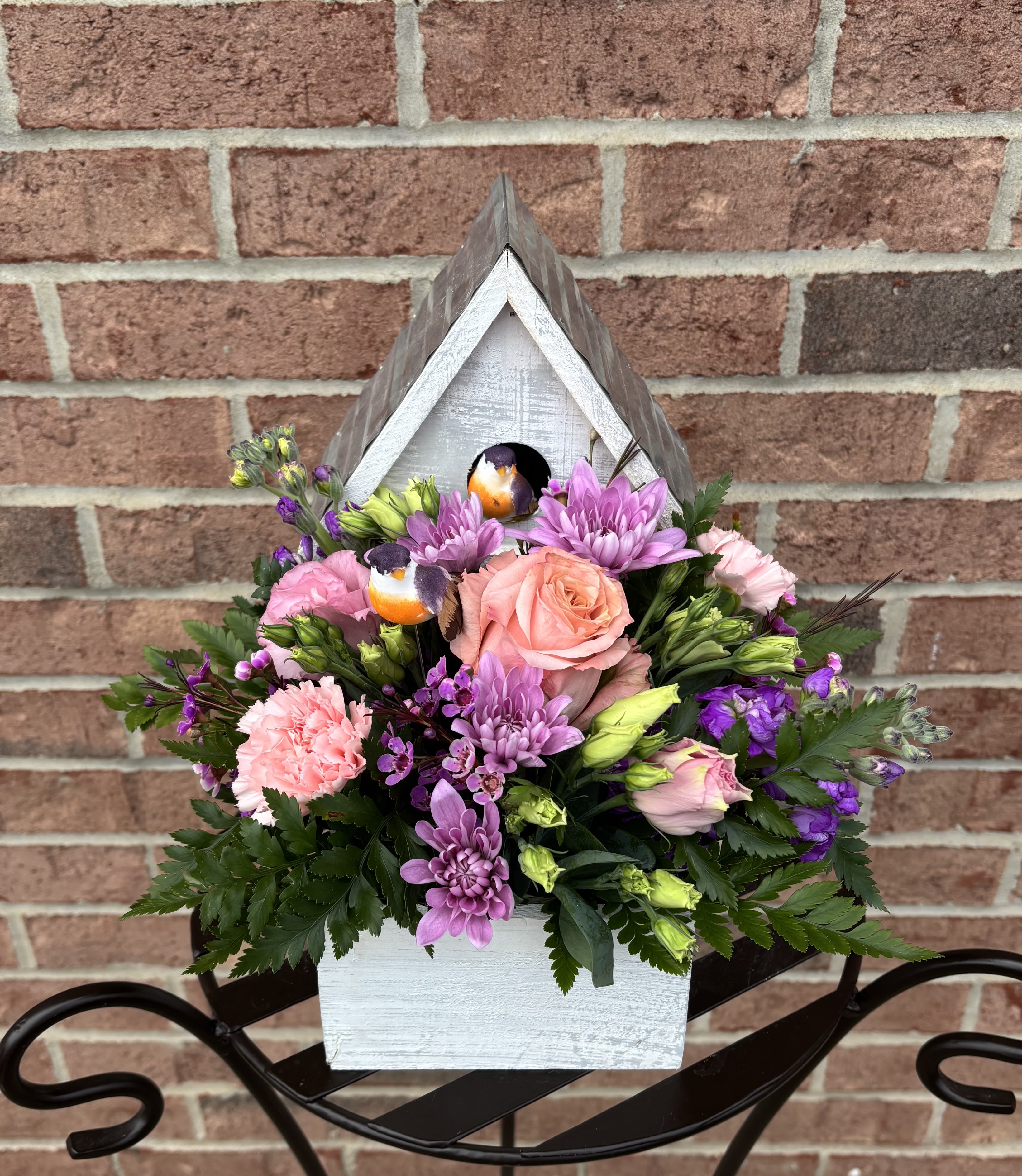 Mixed pink and purple flowers arranged in a white wooden birdhouse planter