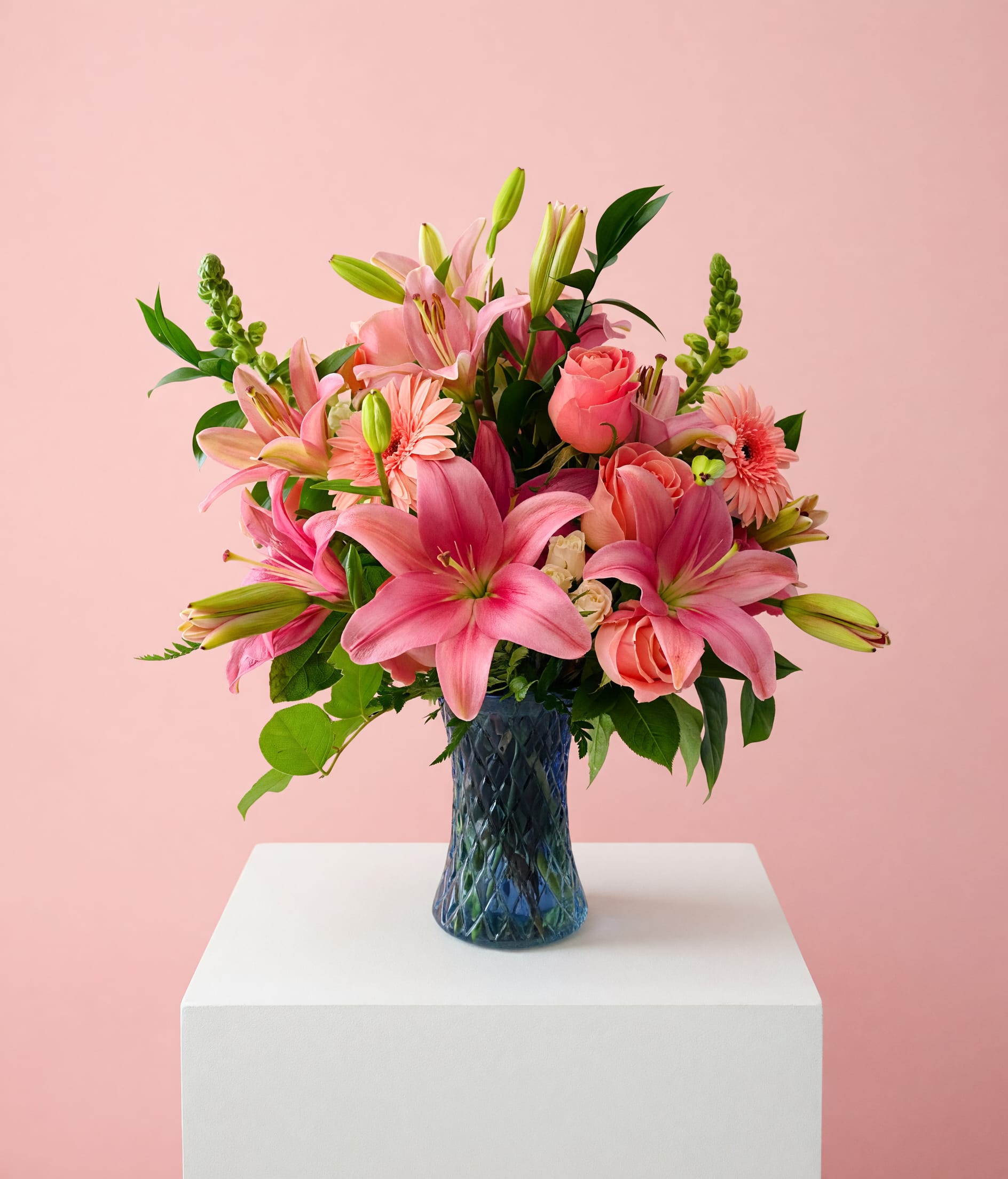 Blushing Lily Embrace for Mom - Celebrate Mom with a graceful arrangement that feels as warm and beautiful as her love. Blushing Lily Embrace for Mom showcases stunning pink lilies in full bloom, complemented by soft blush roses and delicate gerbera daisies, all nestled among fresh, vibrant greenery.  Designed in a textured glass vase, this arrangement brings a touch of elegance and charm to any space. Each bloom is thoughtfully placed to create a full, balanced, and garden-inspired look that feels both fresh and timeless.  Every arrangement is uniquely crafted, ensuring your gift is truly one-of-a-kind—just like Mom. Includes a personalized card message so you can share your love in your own words. Custom requests are always welcome—we’re happy to create something extra special just for her this Mother’s Day. 