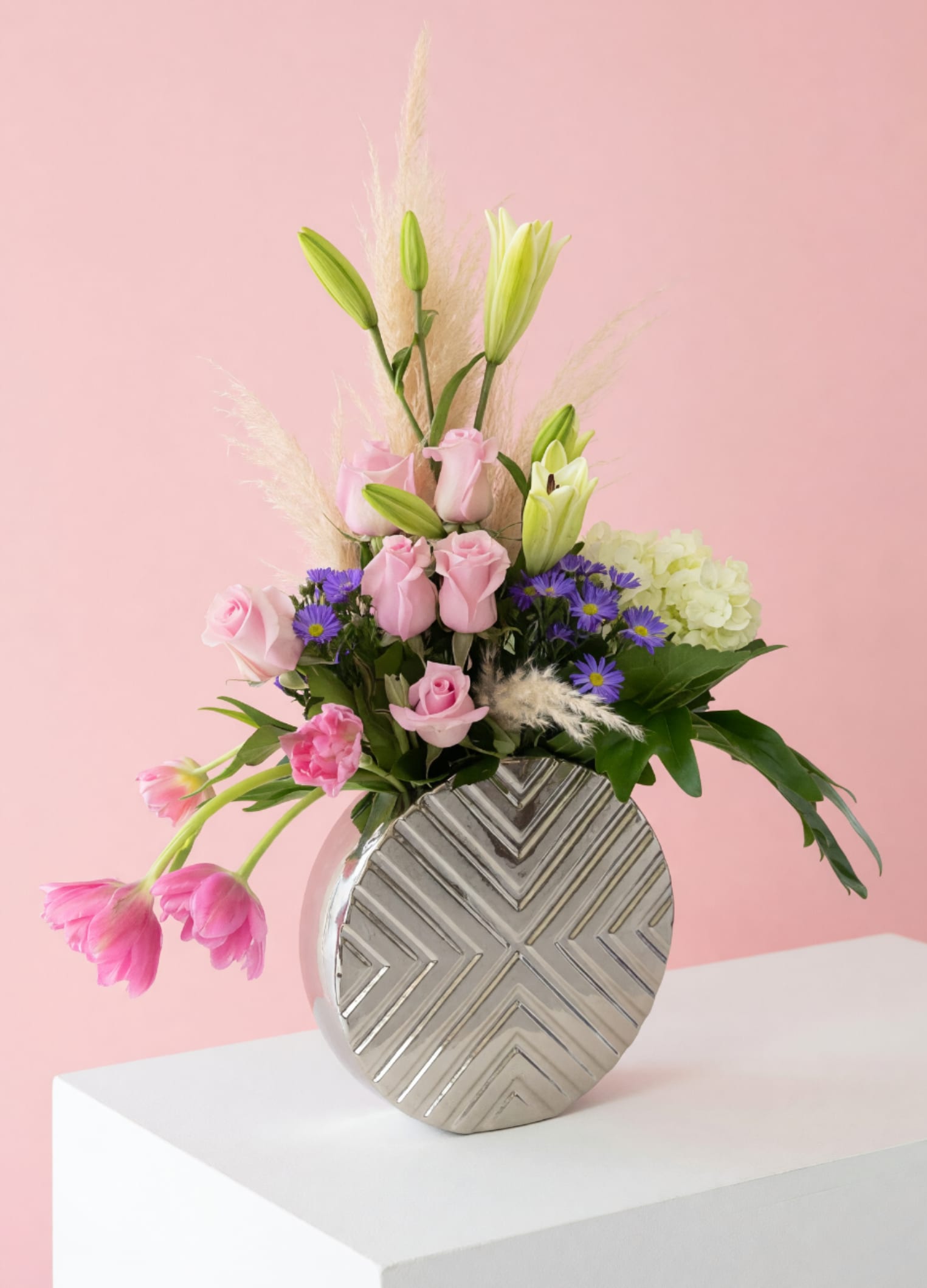 Moms Soft Whispers - Delicate, graceful, and full of charm—Soft Whisper for Mom is designed to celebrate her in the most beautiful way. This arrangement features soft blush roses and elegant lilies, accented with pops of lavender blooms and airy textural elements for a light, modern feel. Designed in a stylish, keepsake vase with a contemporary finish, this piece blends softness with sophistication—perfect for moms who appreciate something unique and thoughtfully curated. Gentle movement from cascading tulips and wispy accents adds an organic, garden-inspired touch. Each arrangement is handcrafted and one-of-a-kind, ensuring your gift is as special as she is. Includes a personalized card message so you can share your love and appreciation this Mother’s Day. Custom requests are always welcome—we’d love to create something just as beautiful and meaningful for you. 