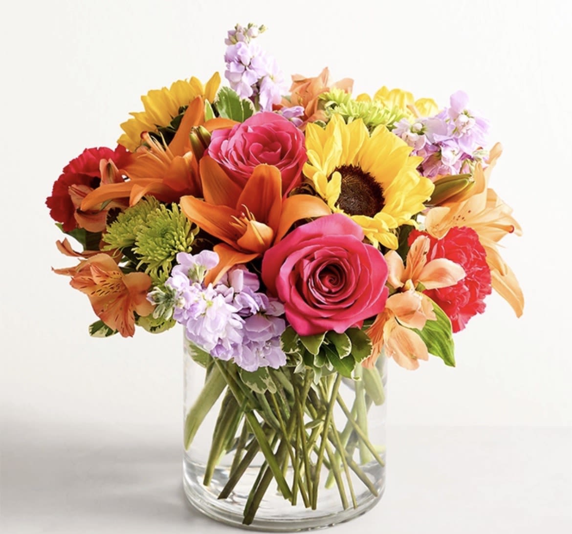 Mixed bouquet of roses, sunflowers, lilies, and carnations in a glass vase