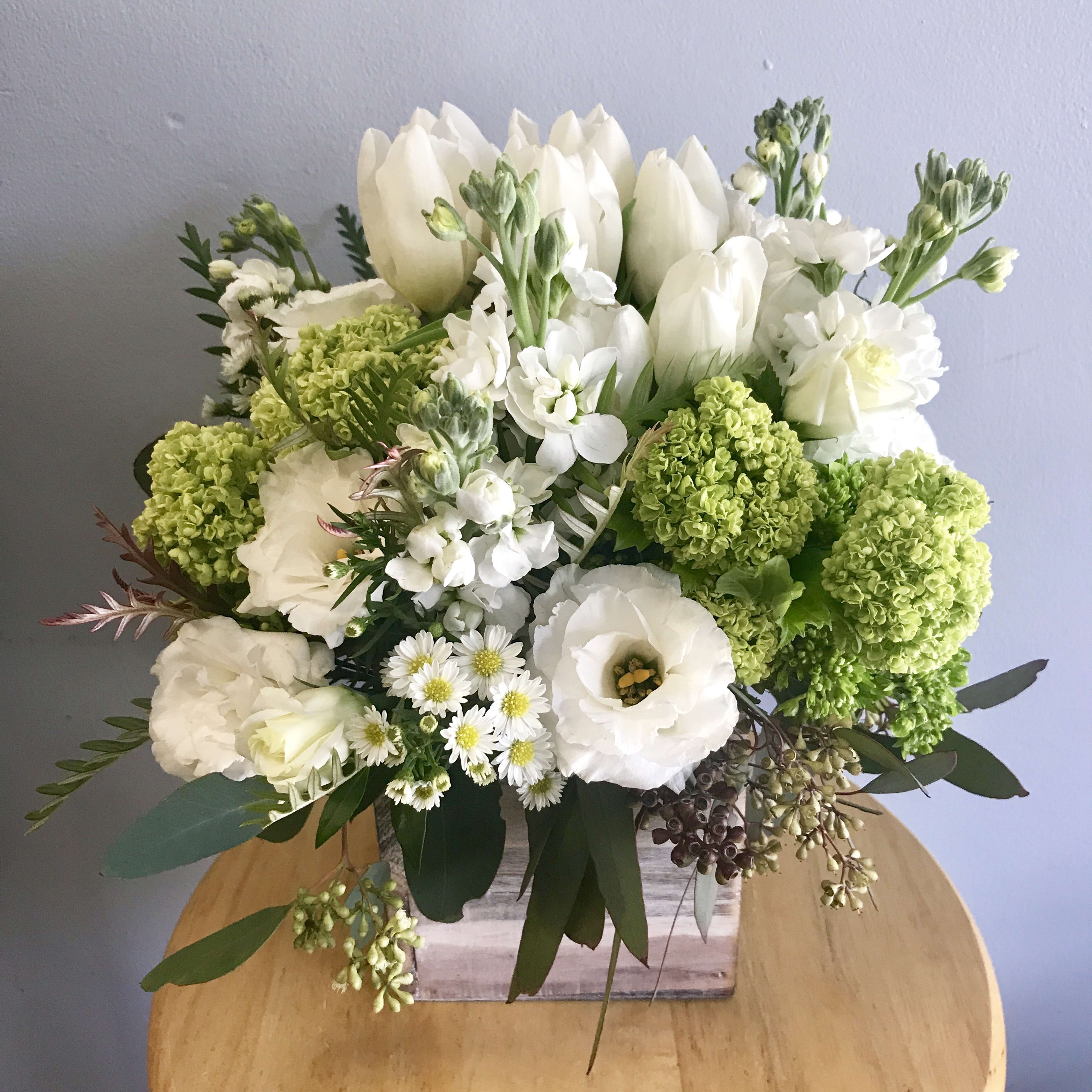 White and green floral arrangement with tulips, lisianthus, and daisies in a rustic wooden cube vase