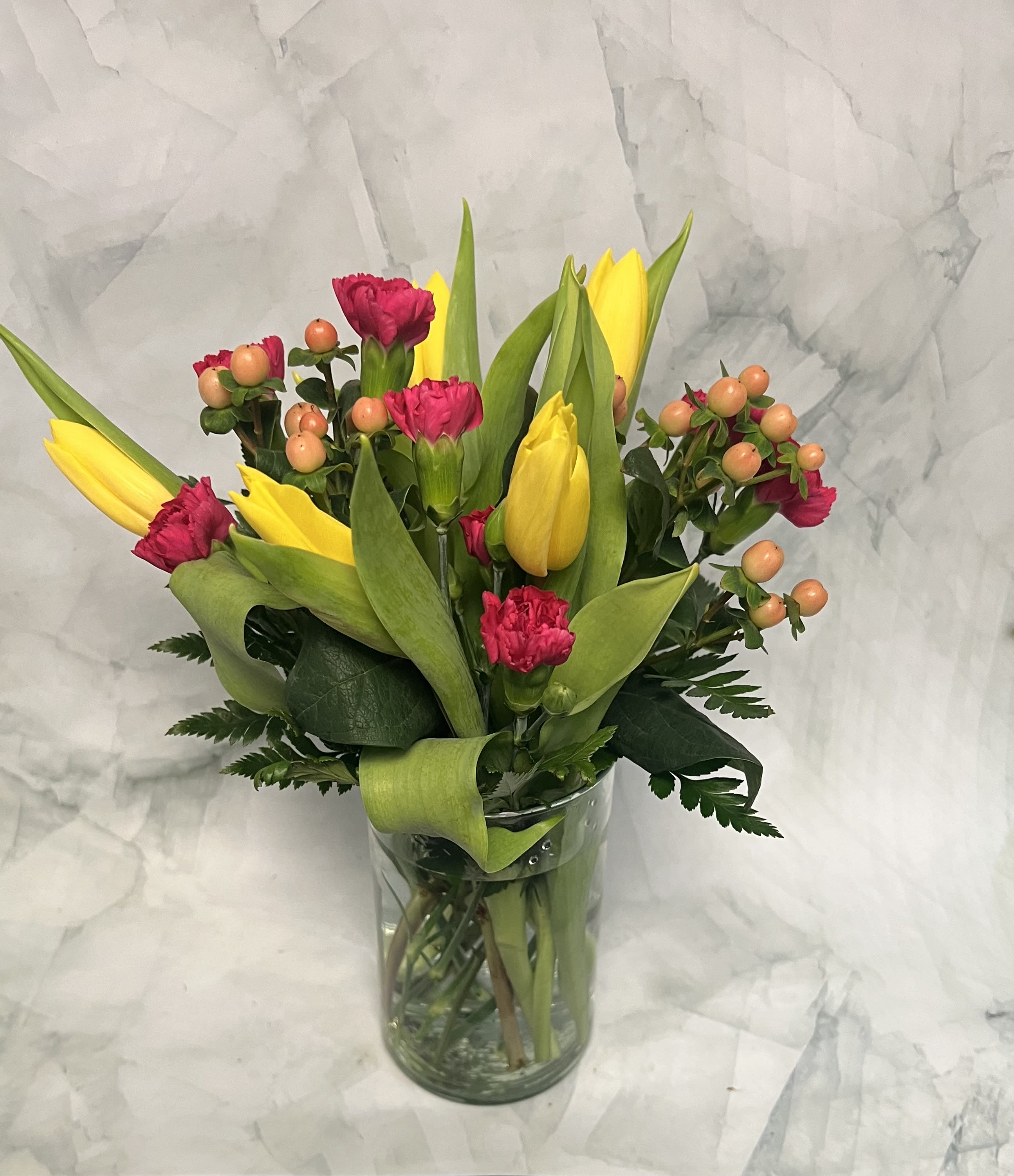 Yellow tulips and pink carnations in a clear glass vase