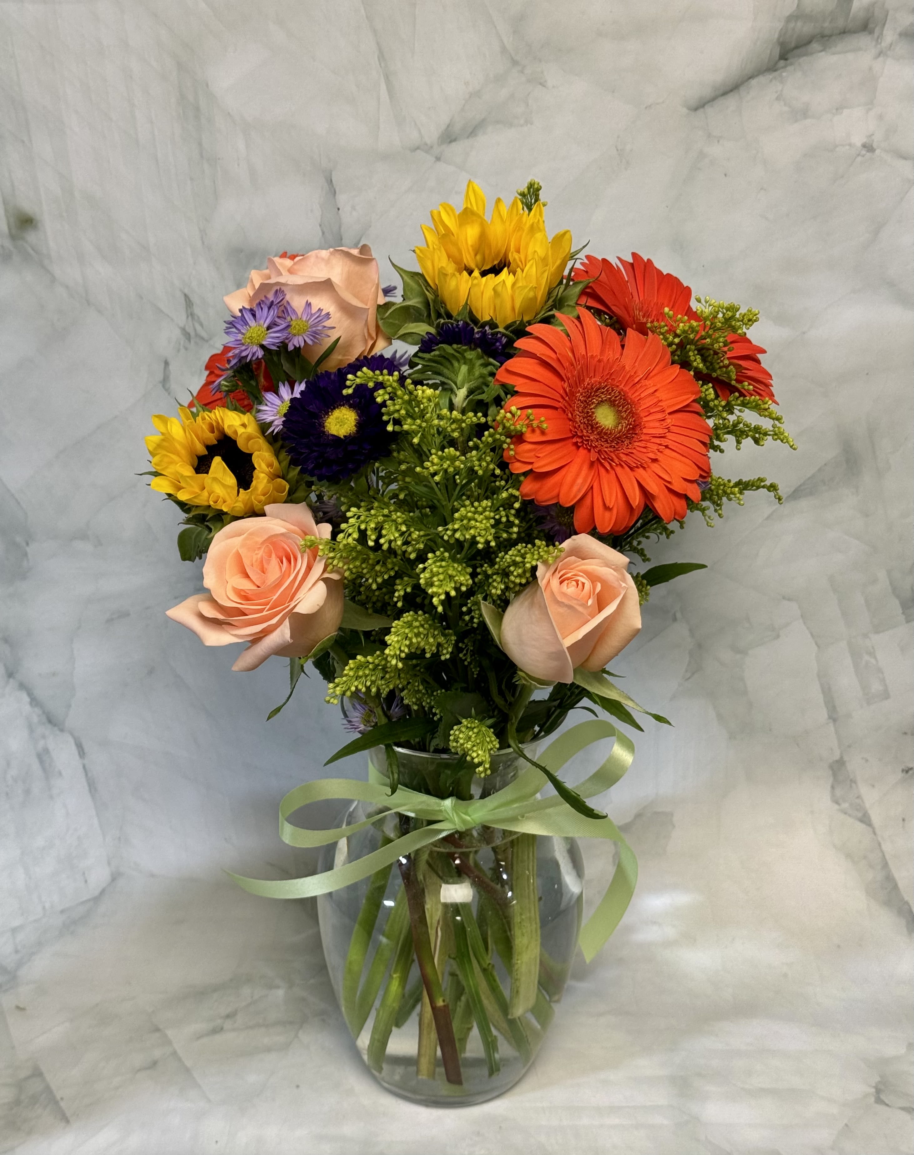 Mixed bouquet of roses, gerbera daisies, and sunflowers in a glass vase