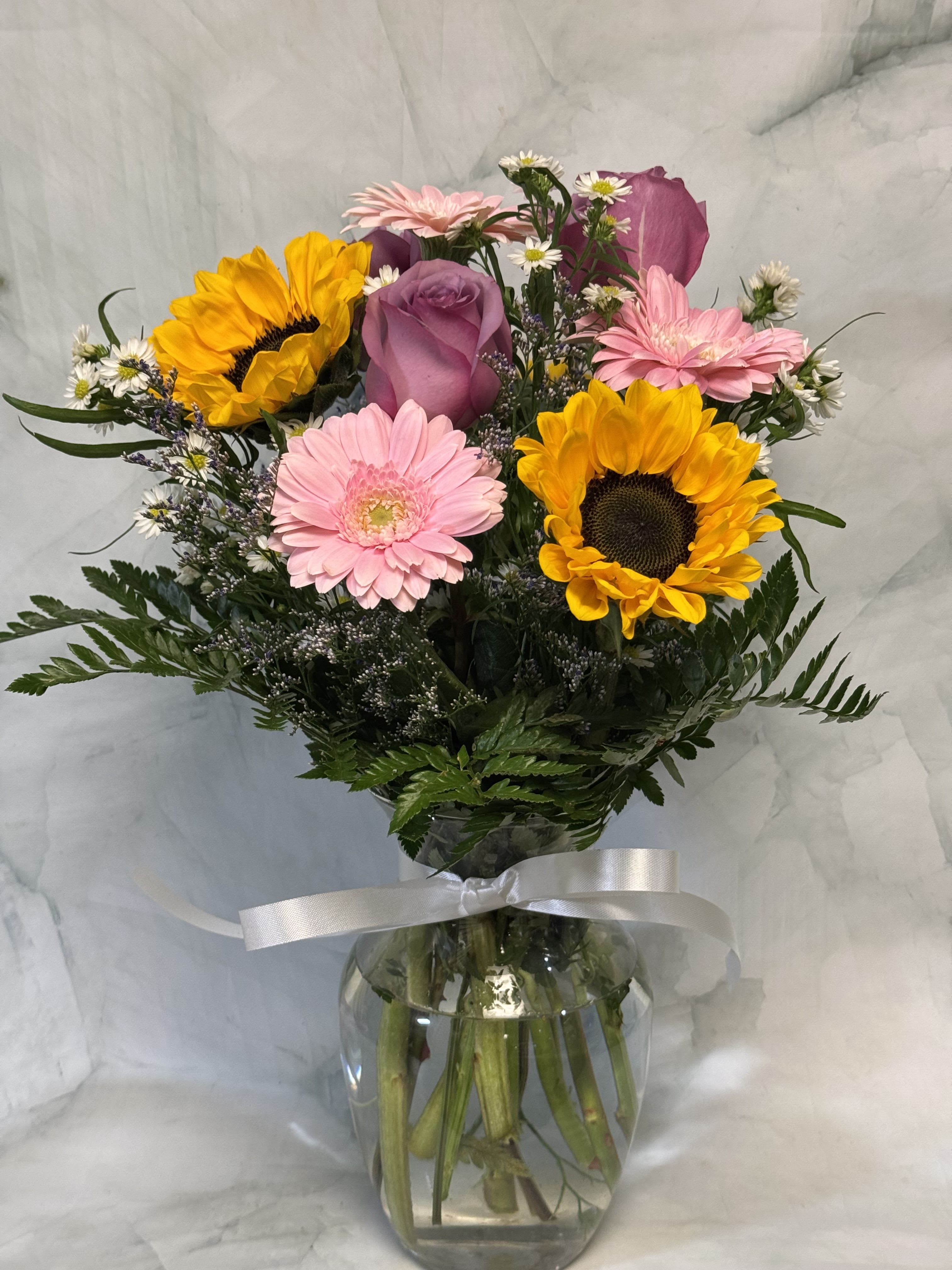 Mixed bouquet with sunflowers, pink gerberas, and a purple rose in a glass vase