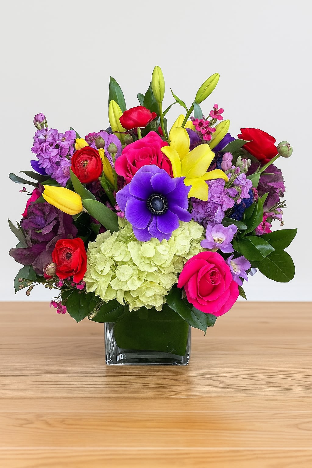 Colorful bouquet in a square glass vase with roses, lilies, and purple blooms
