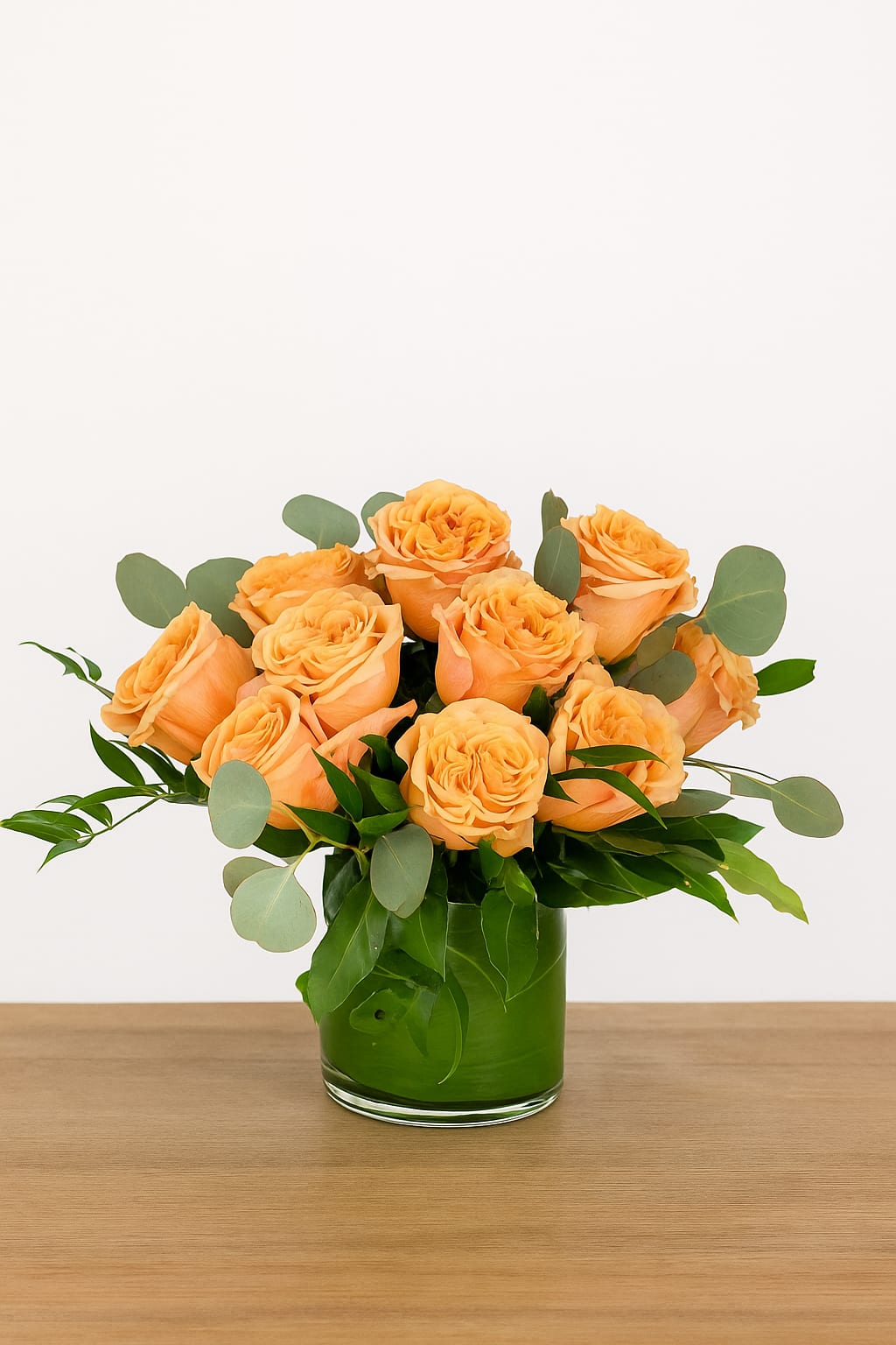 Orange roses in a green glass vase with eucalyptus