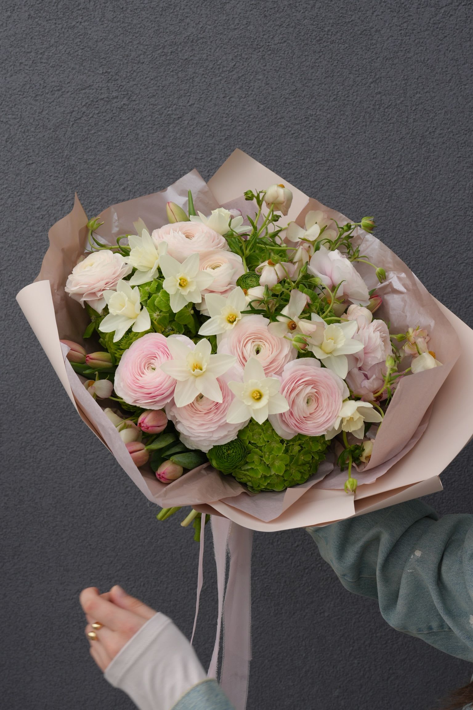 Hand-tied bouquet of pale pink and white flowers wrapped in blush paper