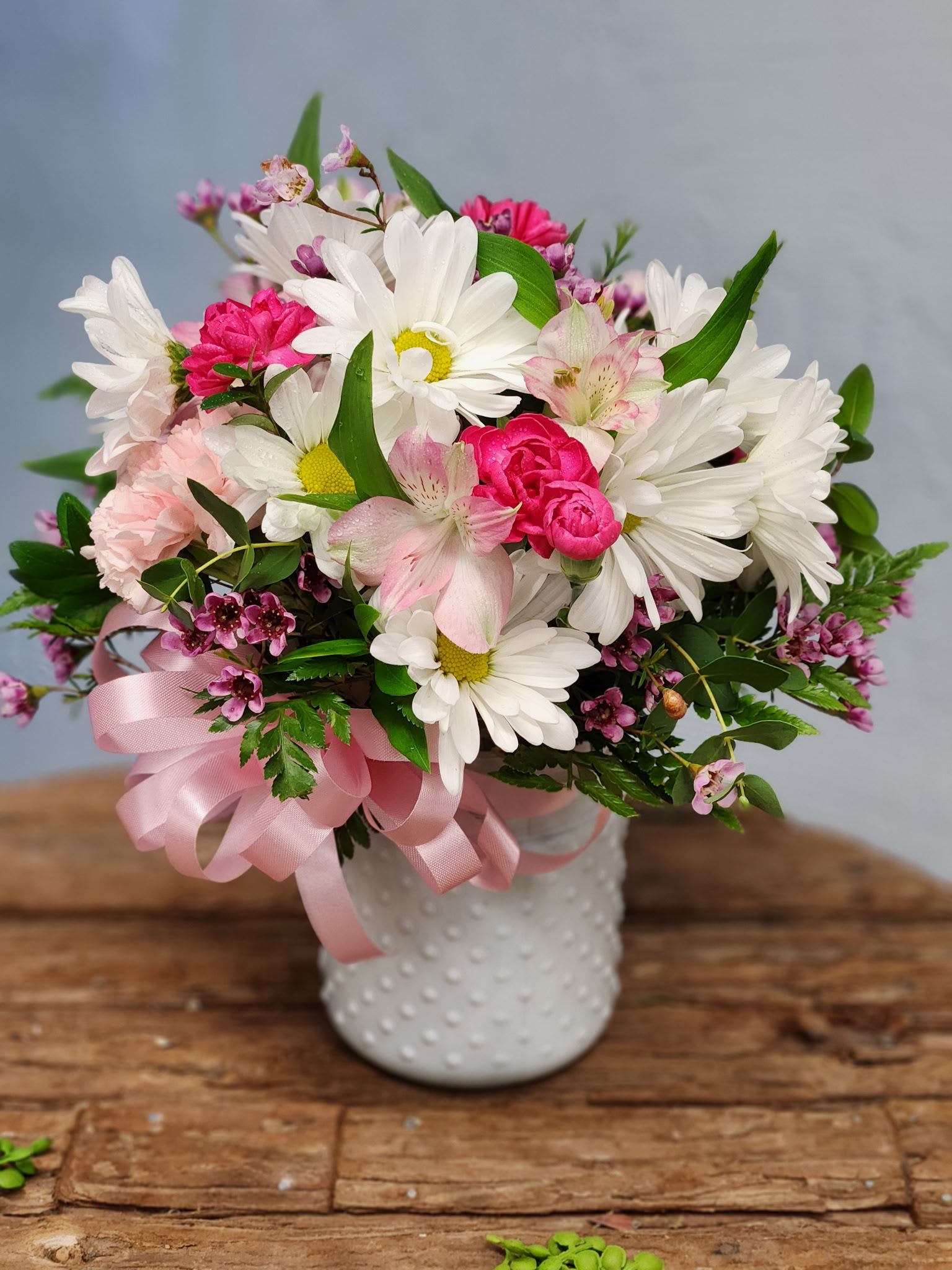 White daisies and pink blooms in a white textured vase with a pink ribbon bow.