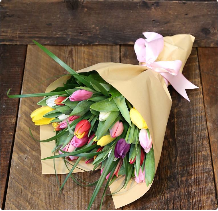Bouquet of multicolored tulips wrapped in tan paper with a pink ribbon