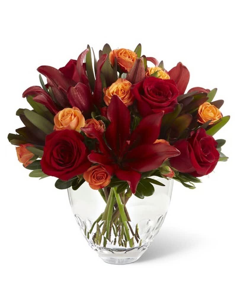 Compact arrangement of red lilies and red and orange roses in a clear glass vase