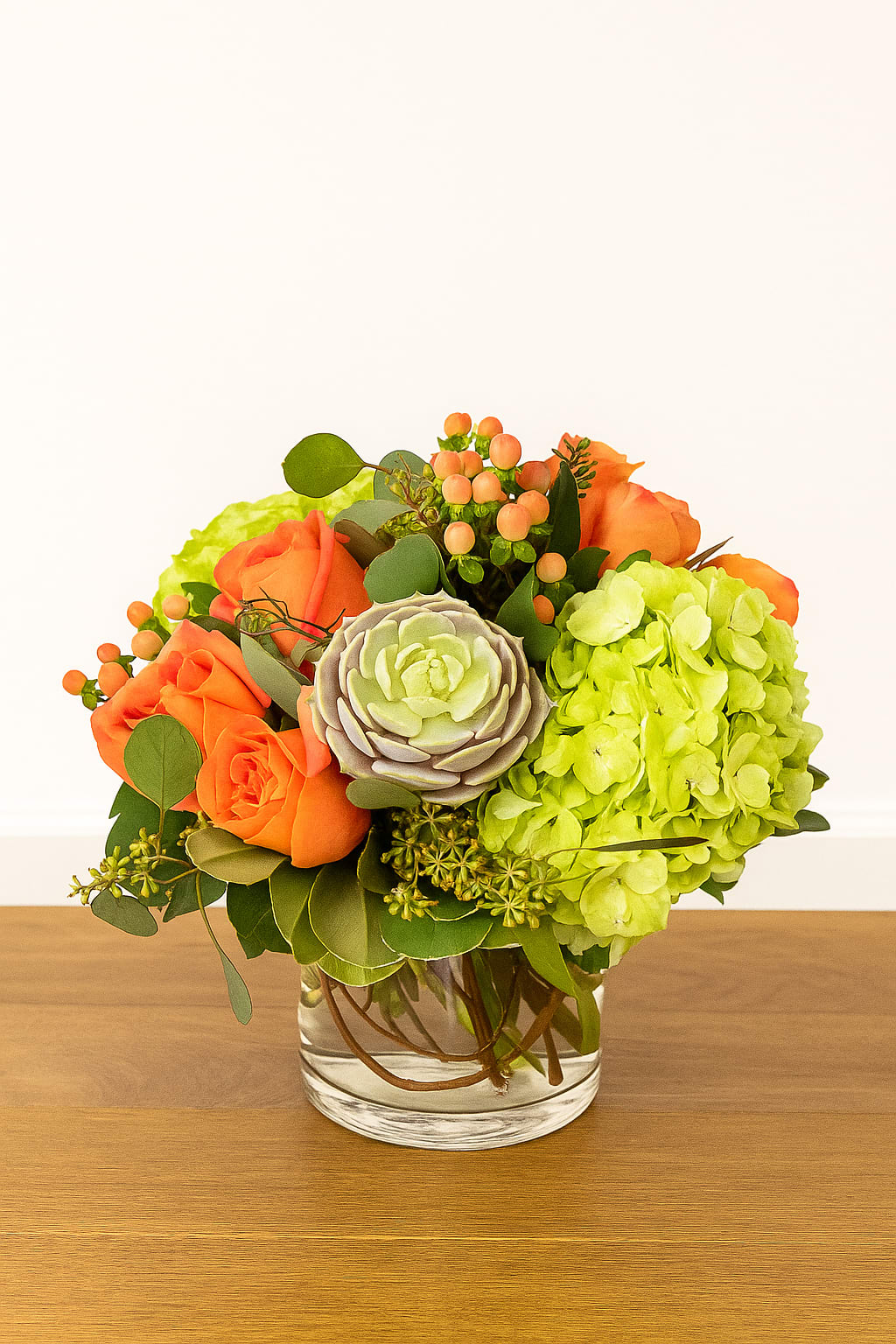 Orange roses and green hydrangea in a clear glass vase