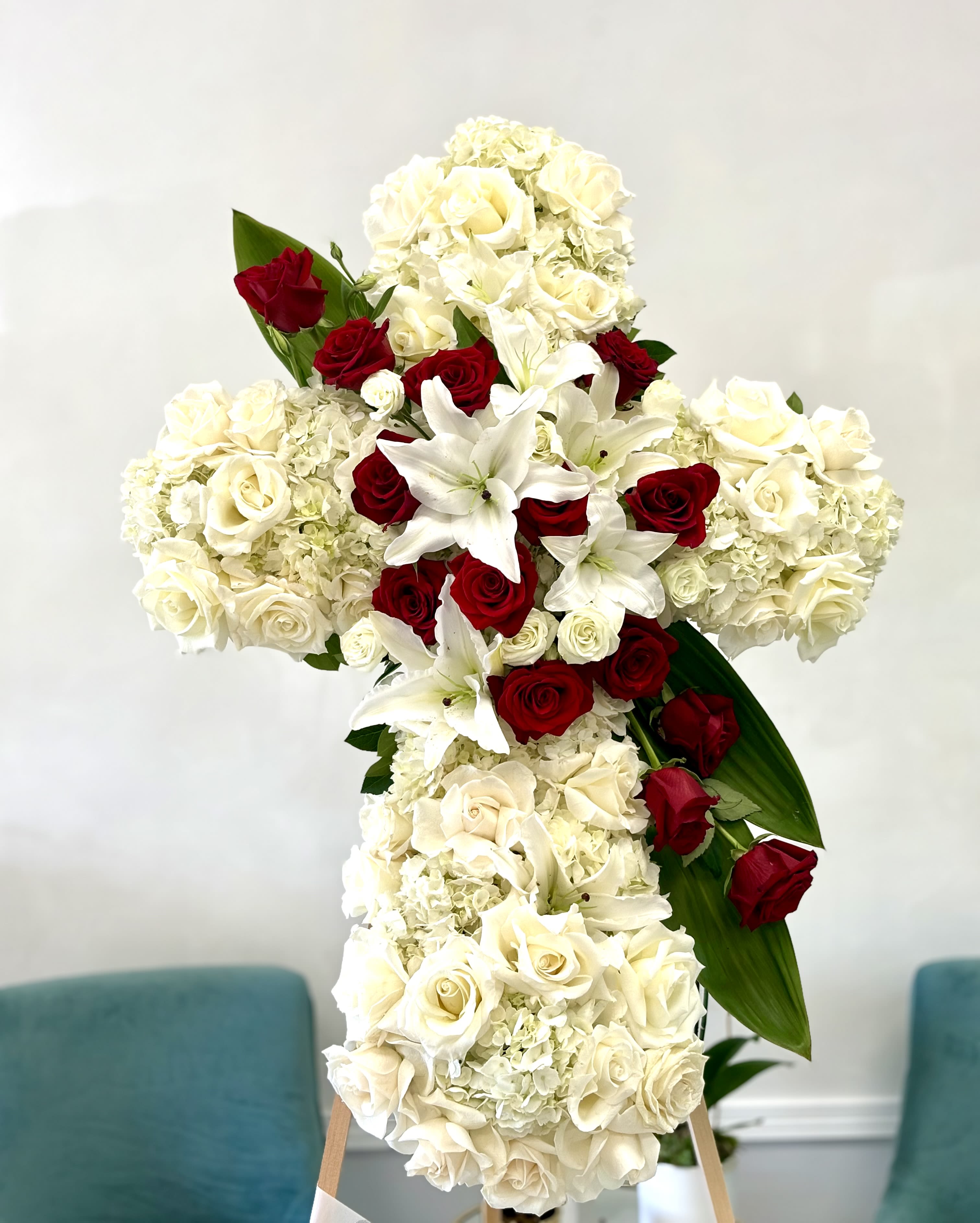 Cross-shaped floral arrangement of white hydrangeas, roses, lilies, and red roses