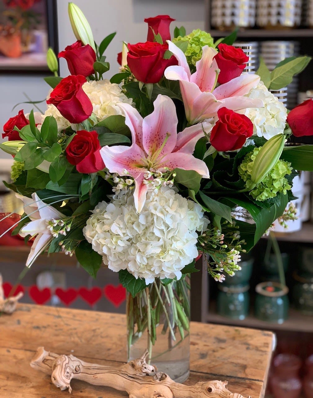 Vase arrangement of red roses, pink lilies, and white hydrangeas in a clear glass cylinder