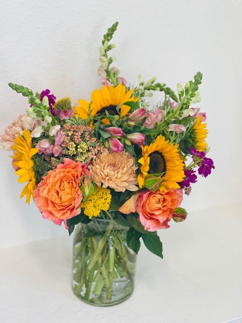 Mixed bouquet with sunflowers, peach roses, and pink blooms in a glass vase