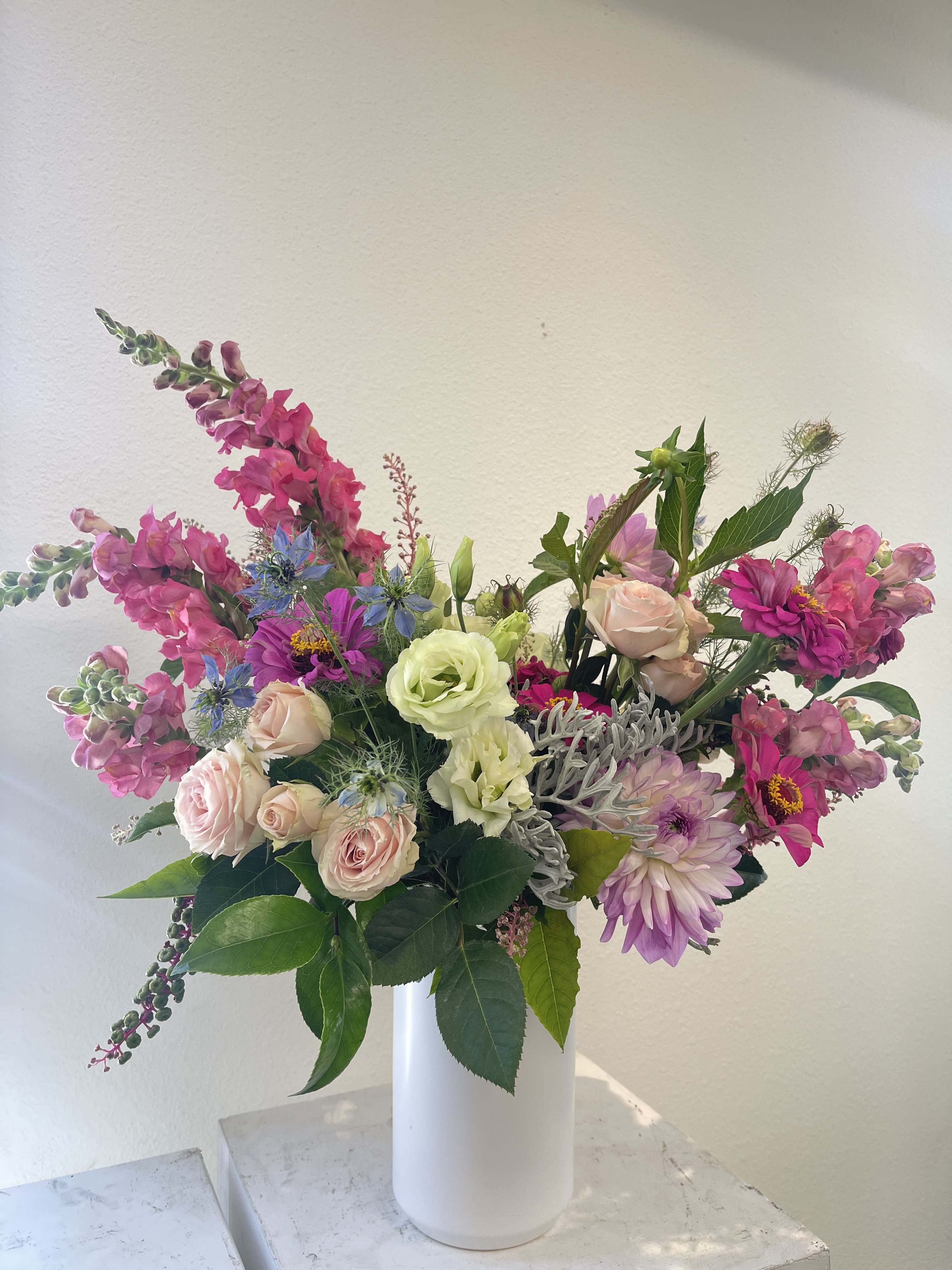 Mixed pink and lavender flowers arranged in a tall white vase