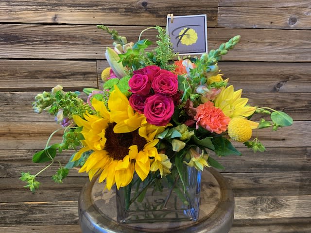 Bright mixed bouquet with sunflowers, pink roses, and yellow blooms in a glass vase.