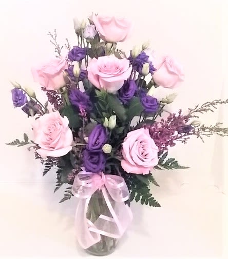 Pink and purple rose bouquet in a clear glass vase with a pink ribbon