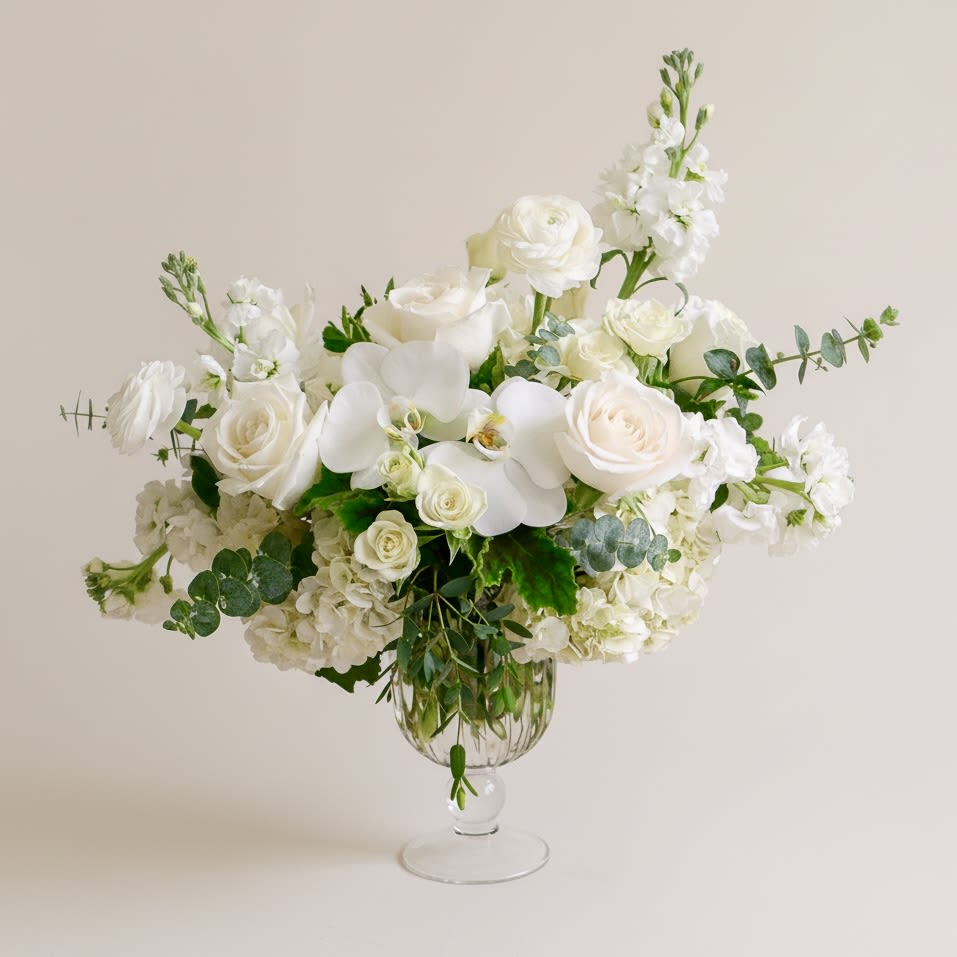 White floral arrangement in a clear glass vase with roses and orchids