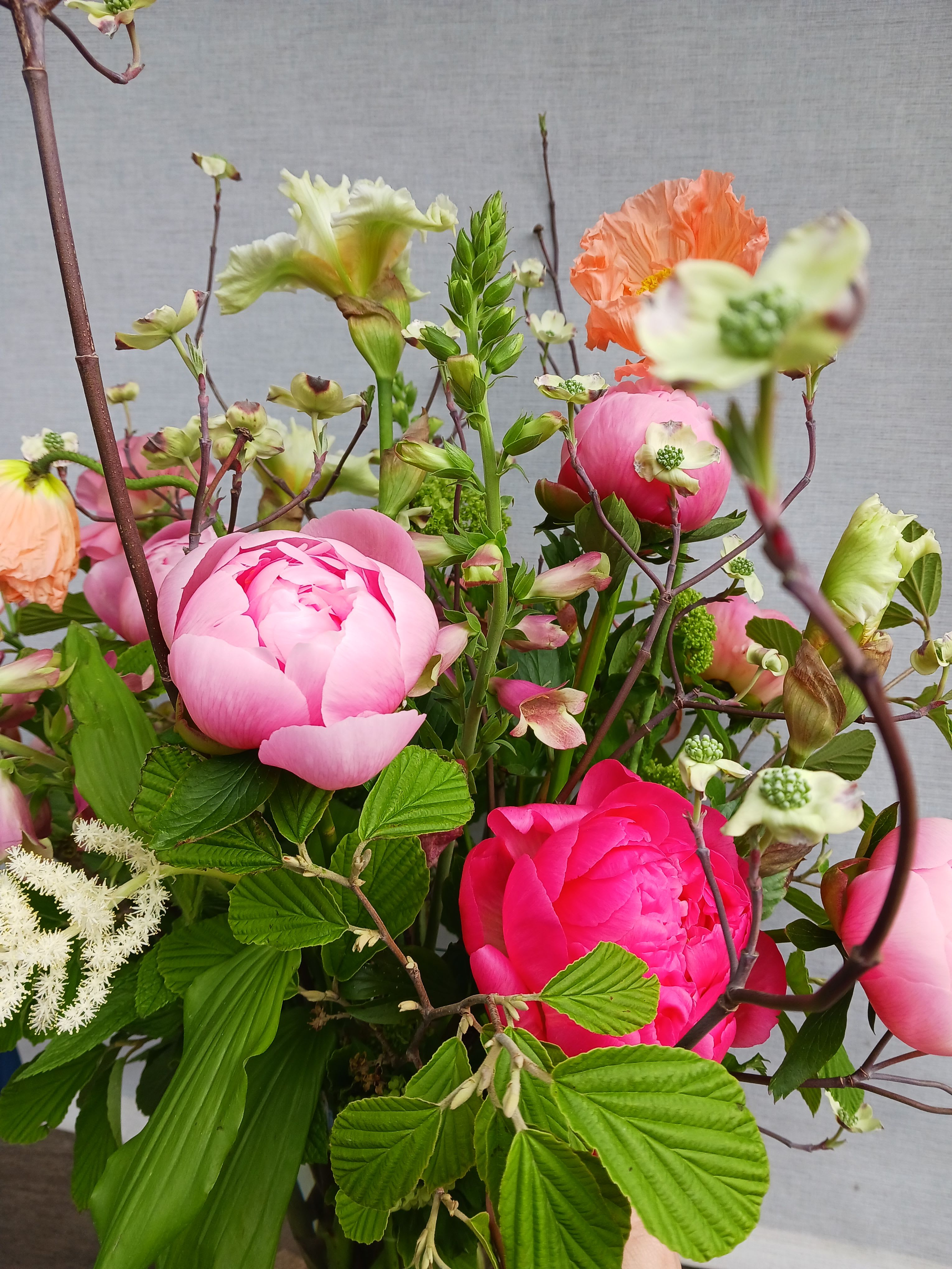 Loose arrangement of bright pink peonies with peach poppies and mixed blooms