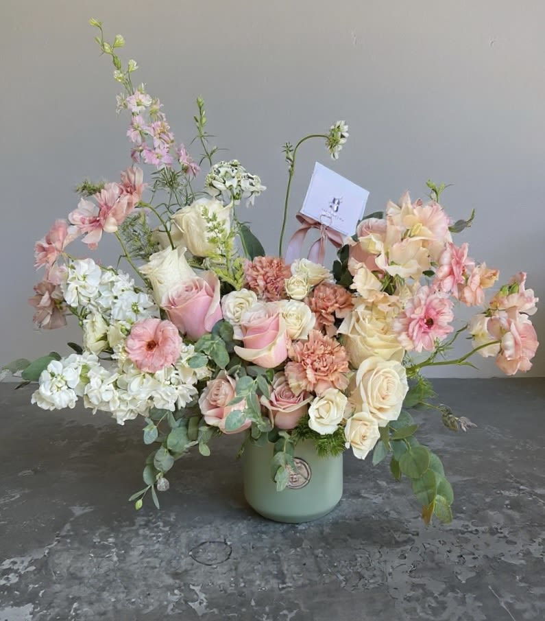 Pastel floral arrangement in a green vase with roses and mixed blooms