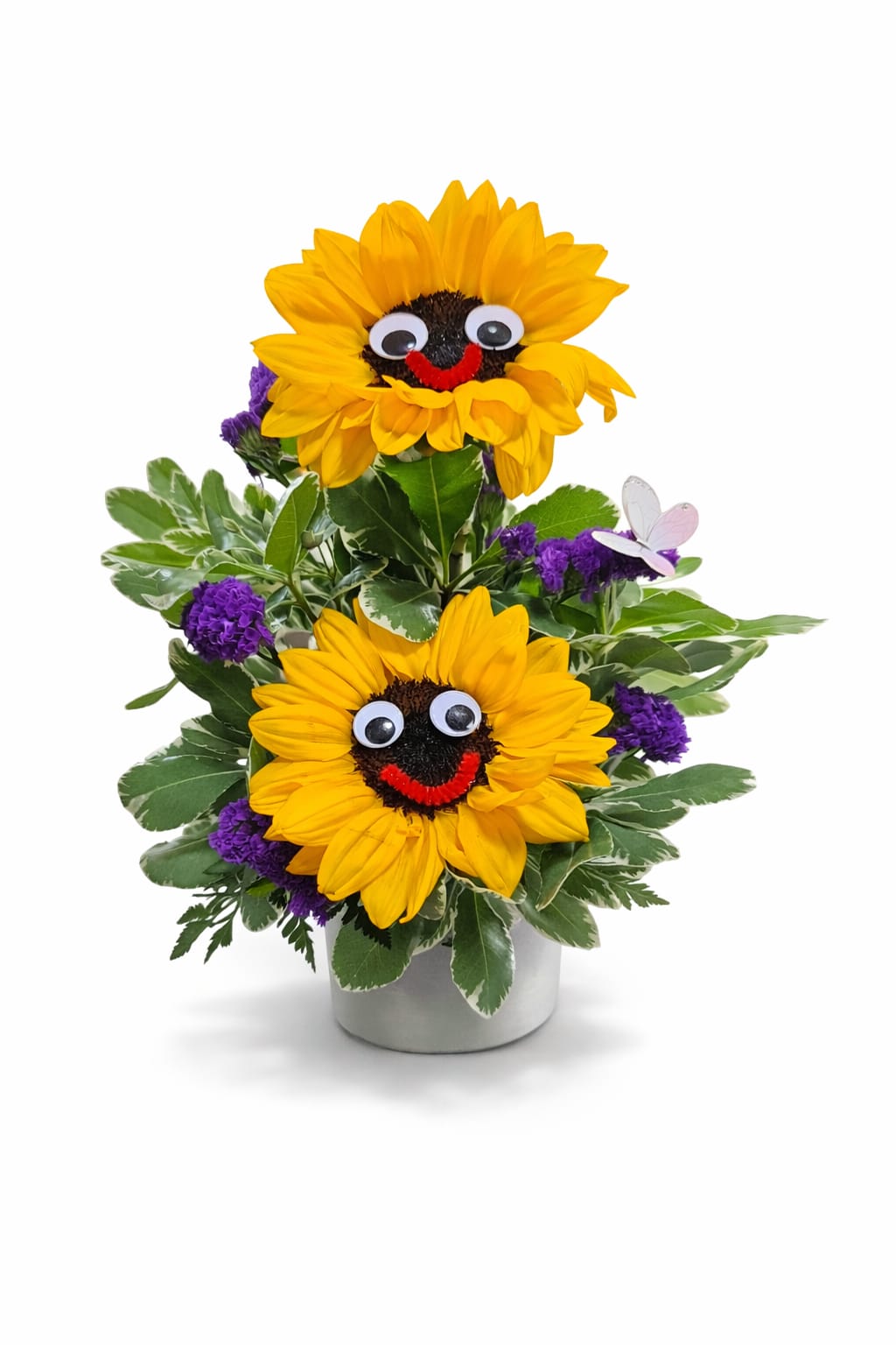 Doble smiley sunshine  - A fun and cheerful arrangement featuring two bright sunflowers with playful smiley faces, surrounded by lush greenery and pops of purple accents. Perfect for birthdays, kids, get-well gifts, or anyone who needs a little extra happiness in their day ️