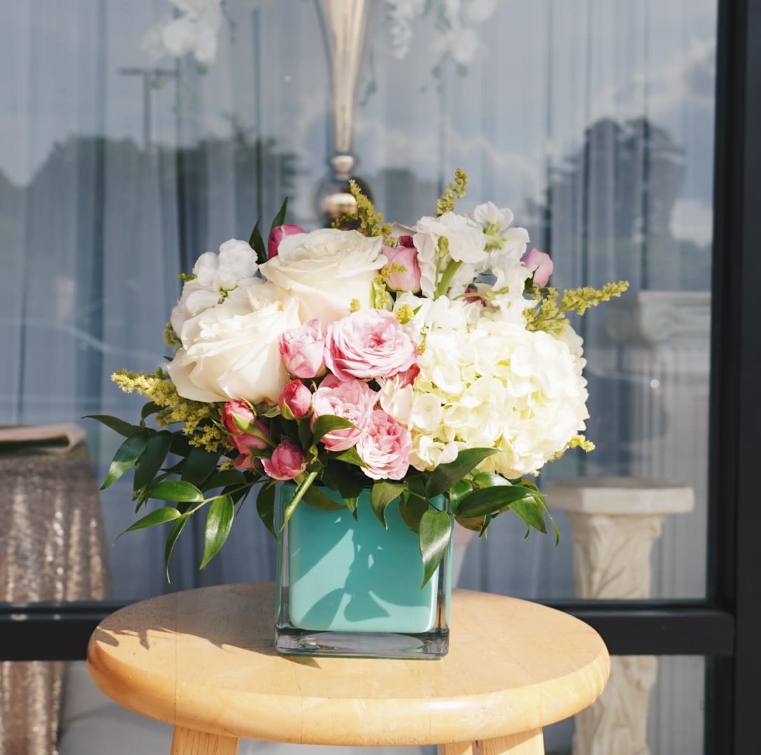  AQUA DREAM BOUQUET BY ATLANTA'S FINEST FLOWERS  - A soft cluster of blush-pink roses and creamy white hydrangea-like blooms framed by bright yellow asters makes a refreshing statement for a birthday bouquet or a spring and summer surprise. This flower arrangement-ideal for Mother's Day or to celebrate a special woman on Women's Day or Best Friends Day-lands as both romantic and cheerfully modern, the kind of gift that will make her feel truly seen.  The arrangement pairs white roses, light pink spray roses, white stock, and white hydrangea-style flowers with yellow aster accents and touches of green for texture. All stems are arranged in a polished 5" x 5" aqua cube (square glass) vase that echoes the cool blue-green tones and gives a contemporary finish. The finished size is approximately 10" x 10", a generous, rounded silhouette that fills a table without overwhelming it.  Perfect for birthdays, Boss's Day, Admin Professionals' Week, or as a Spring or Summer centerpiece, this bouquet arrives ready to display-simple water care will keep the blossoms fresh longer: change the water every couple of days and trim stems as needed. It's a graceful, uplifting choice when you want her to feel celebrated.