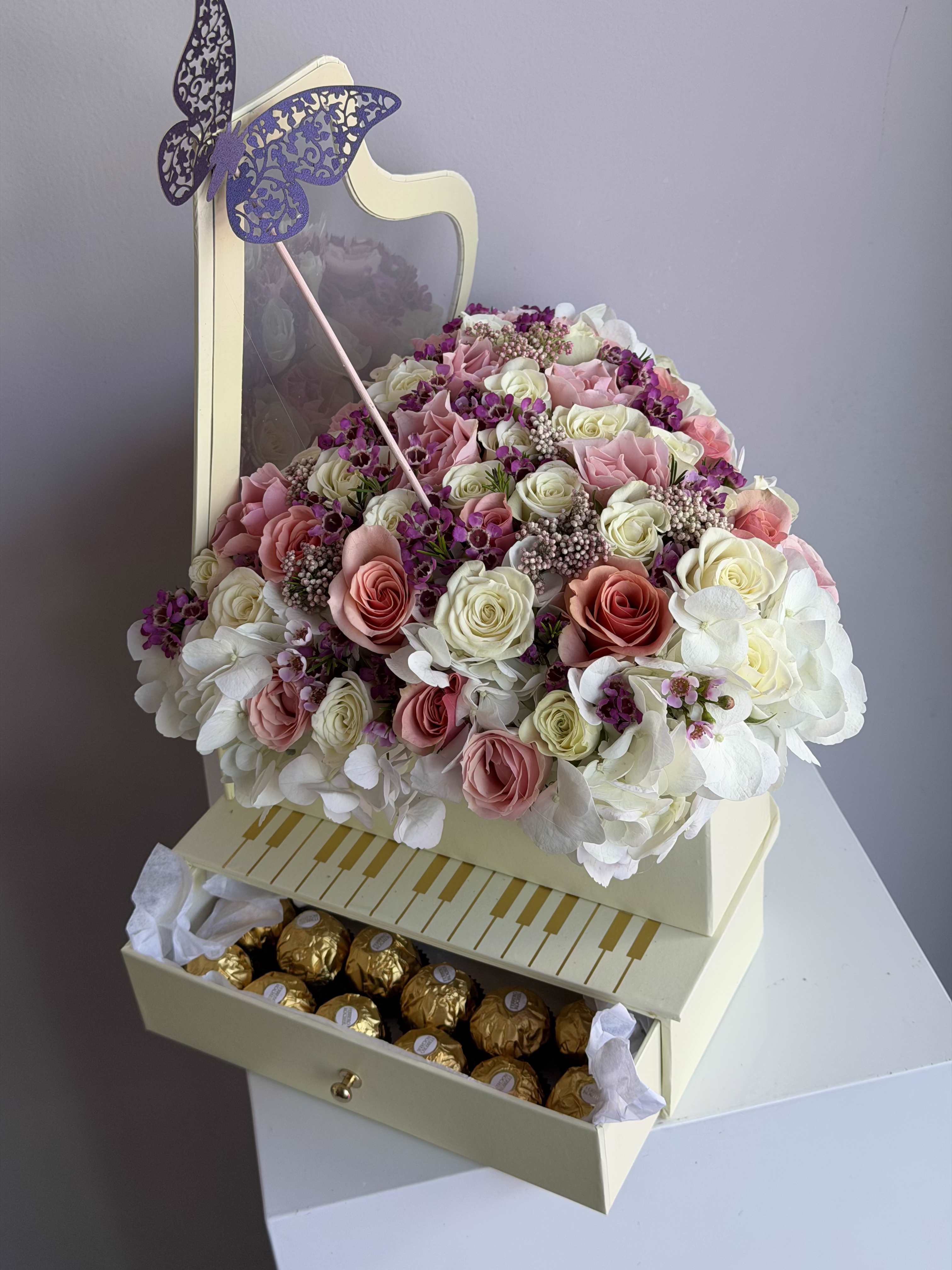 Heart-shaped box of pink and white roses with chocolates in a drawer and a purple butterfly decoration.