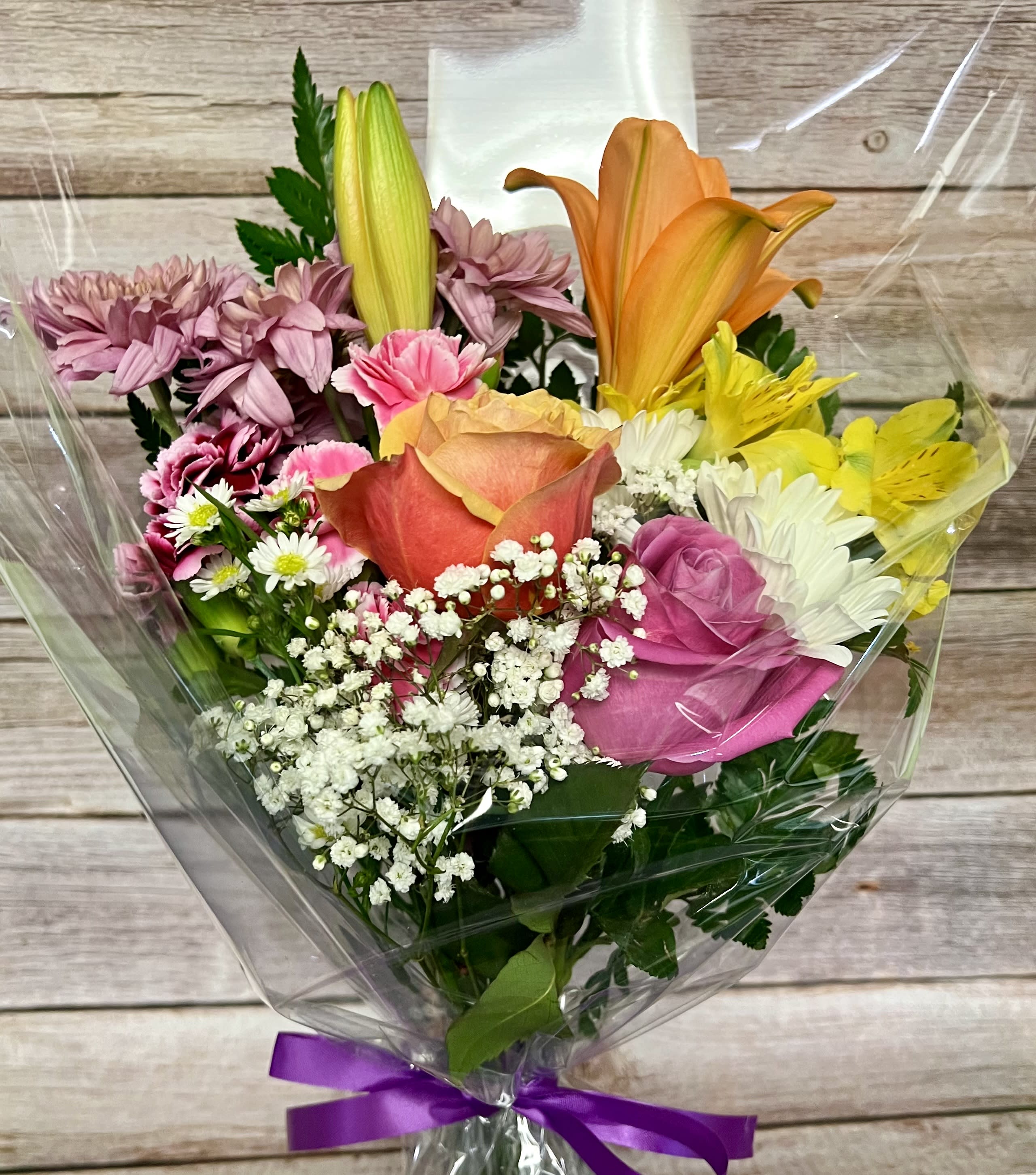 Mixed bouquet with roses, lilies, daisies, and carnations in clear wrap