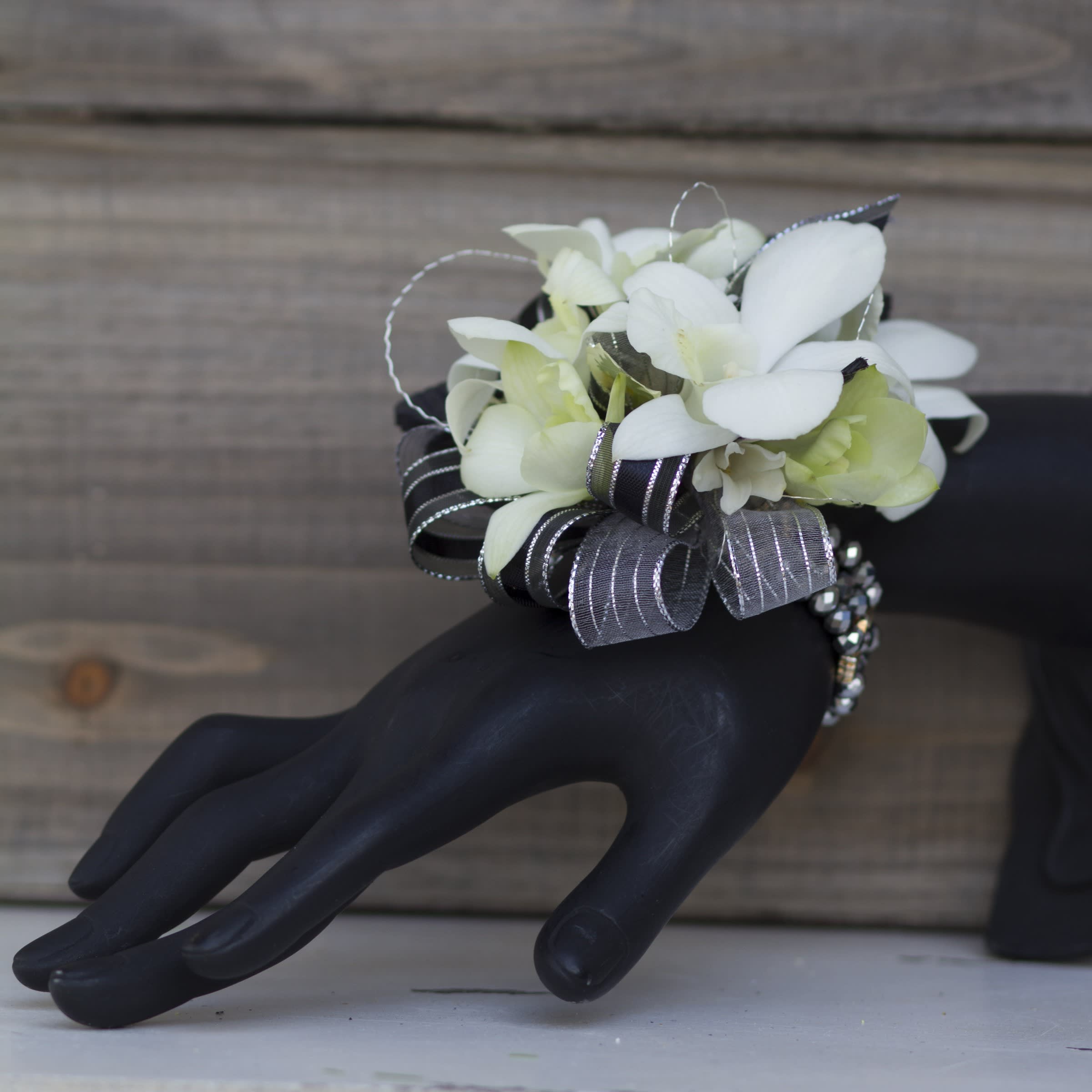White floral wrist corsage with black and silver ribbon on a black hand display