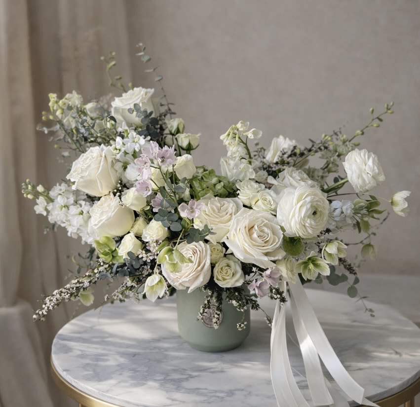 Whimsical Whites - Elegant and enchanting, Whimsical Whites is a dreamy arrangement of delicate white blooms and lush greenery. With a soft, ethereal charm, this design exudes grace and serenity, making it perfect for any occasion that calls for timeless beauty and sophistication. Blooms will vary upon availability.