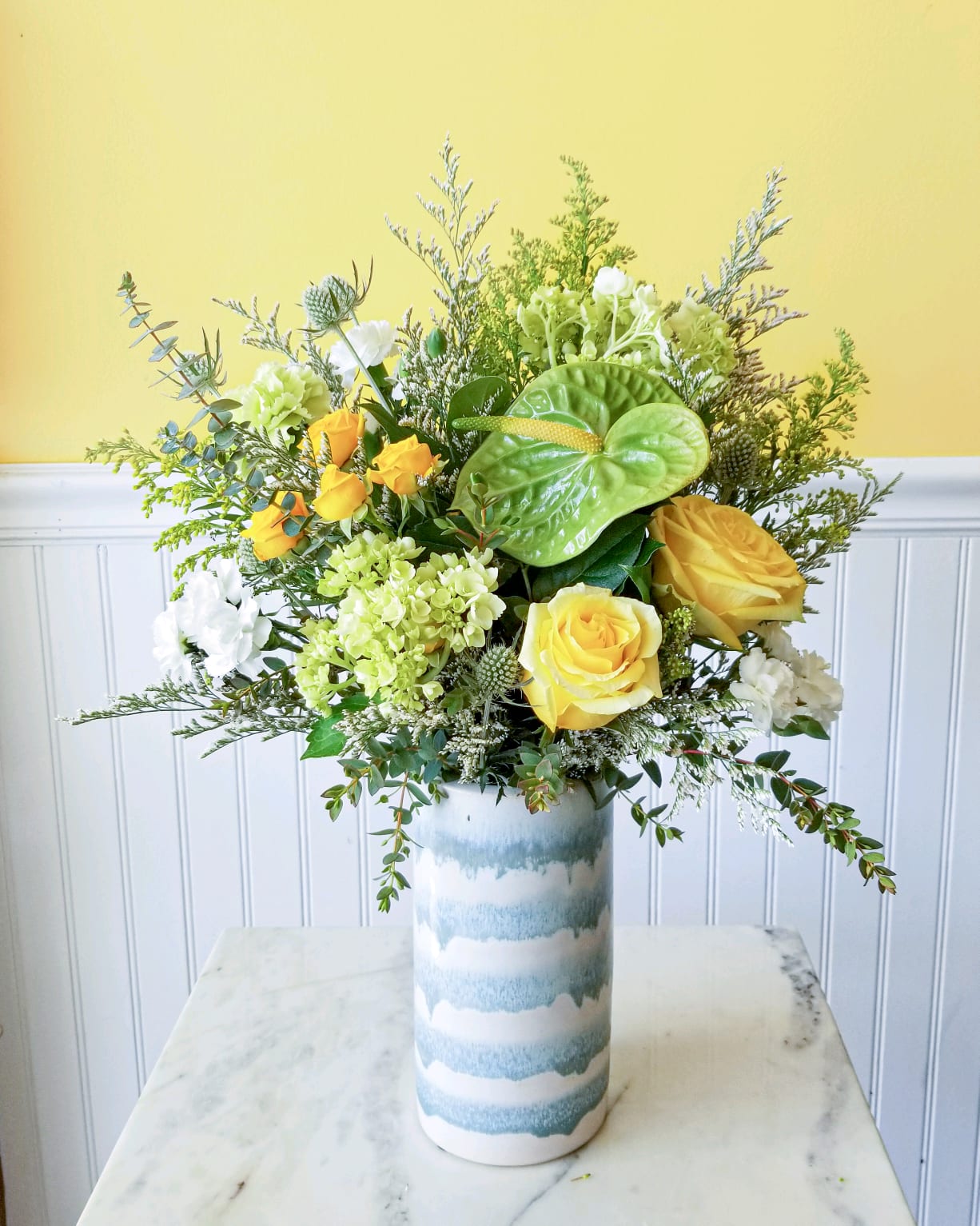 Yellow roses and white blooms in a tall striped vase