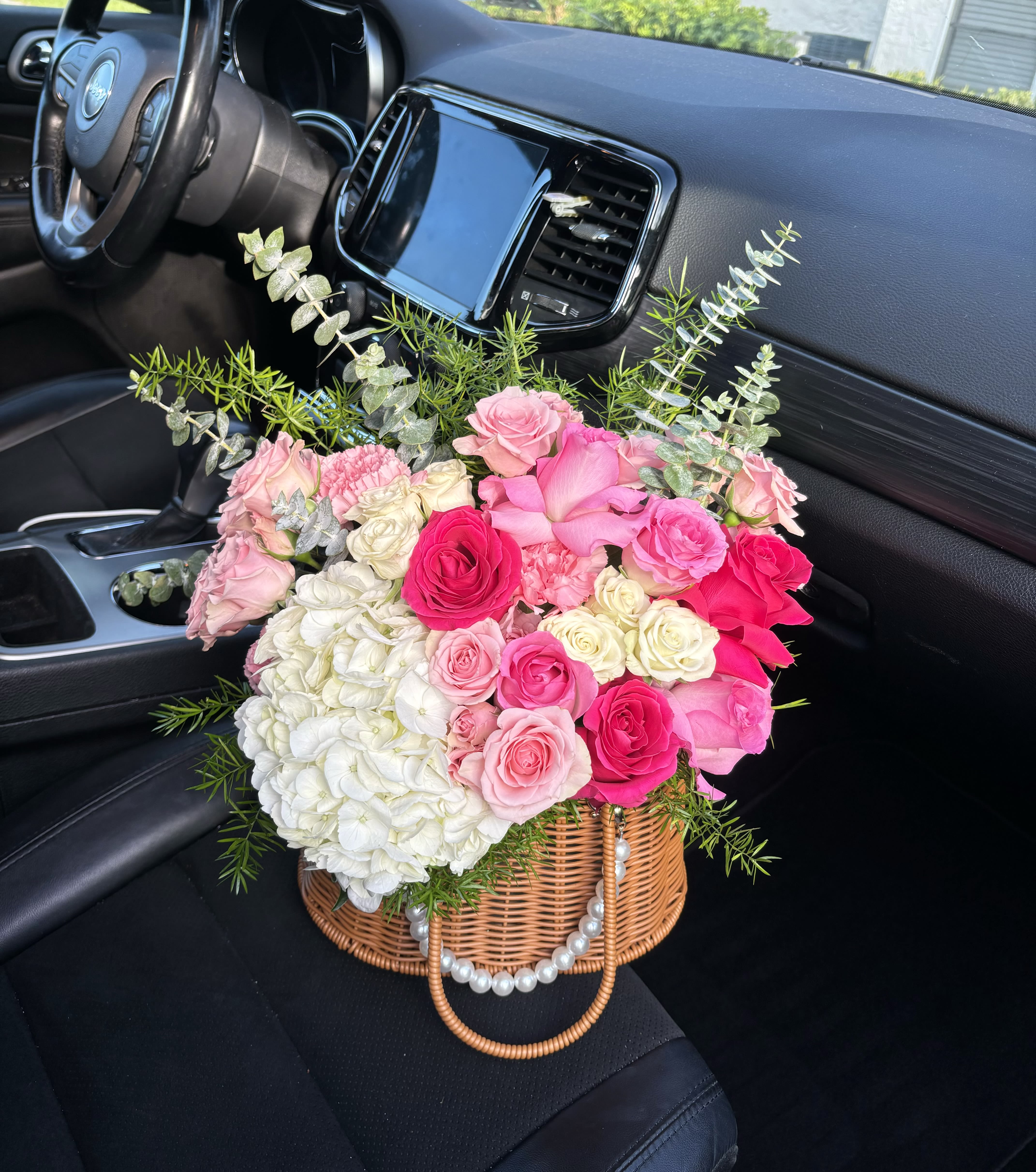 Pink and white rose bouquet in a wicker basket with greenery