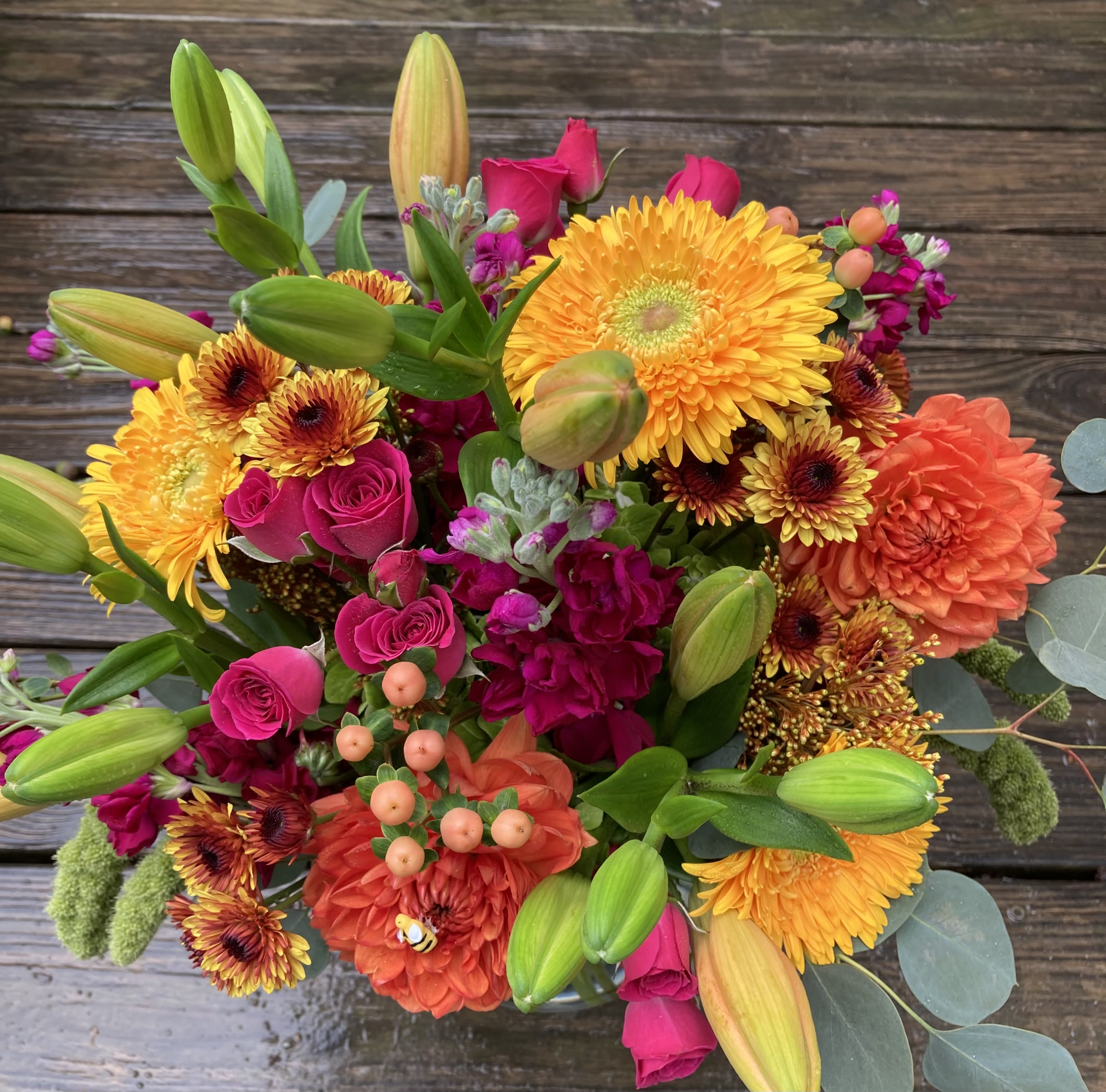 Bright mixed bouquet with yellow daisies, pink roses, orange blooms, and lily buds