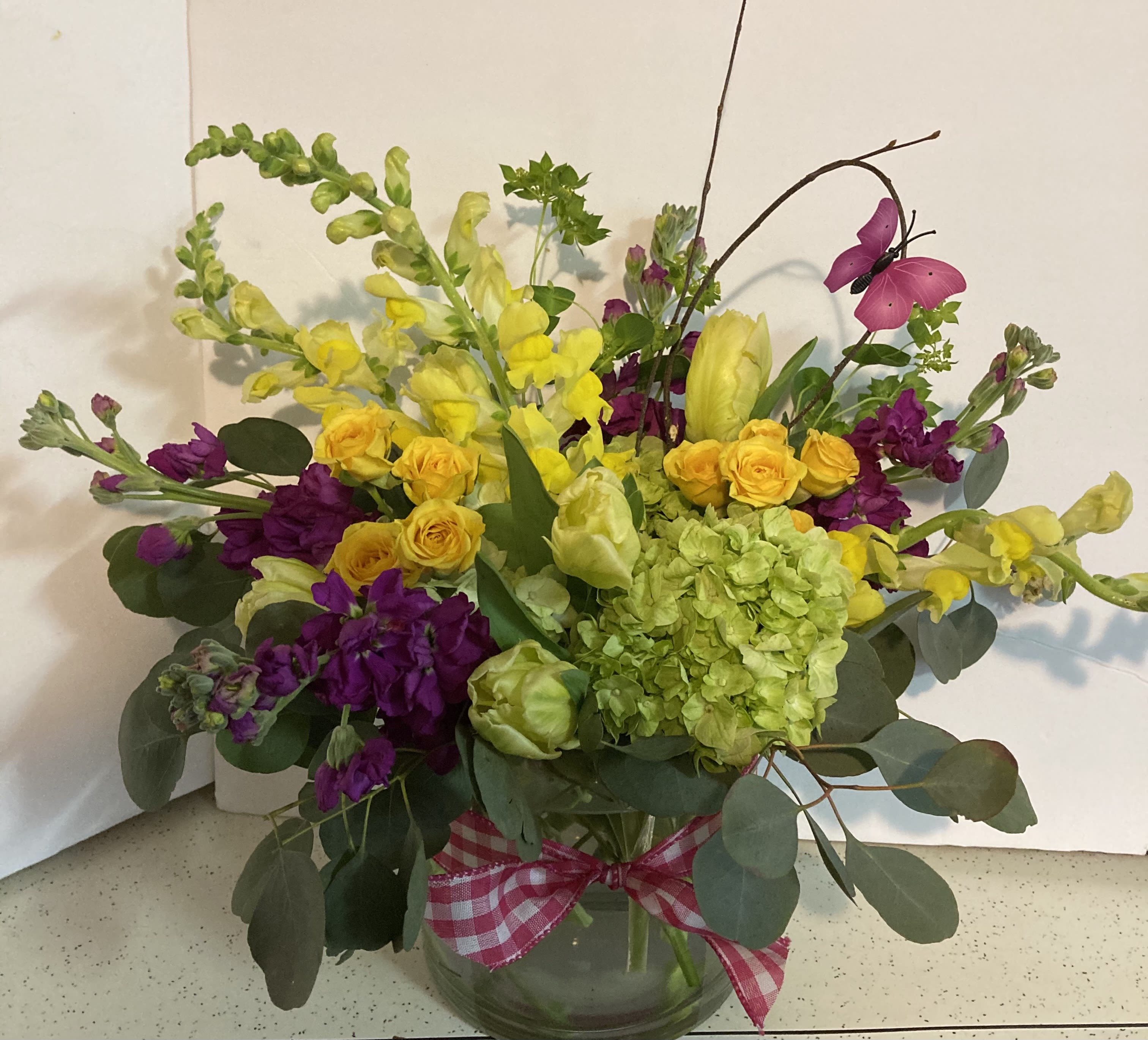 Bouquet of yellow and purple flowers in a glass vase with a pink ribbon