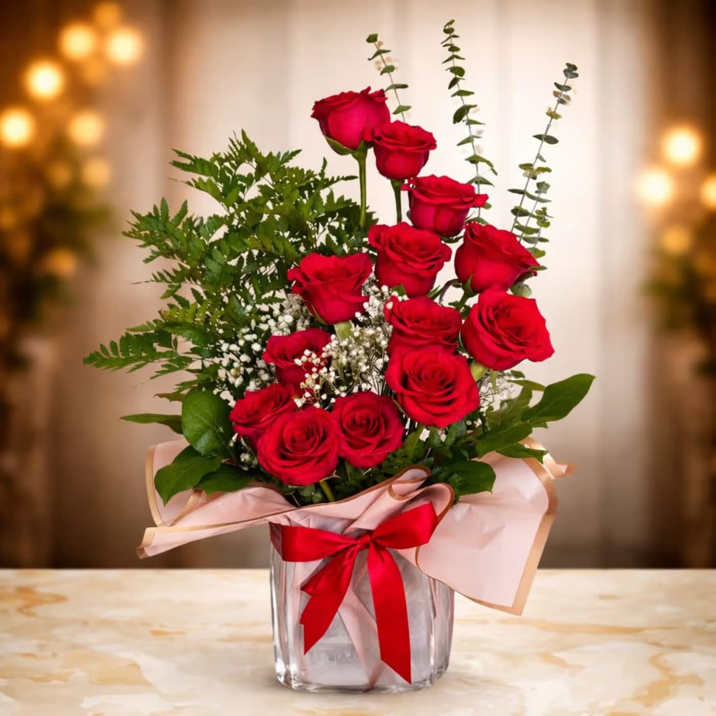Red roses arranged in a clear glass vase with pink wrap and a red ribbon