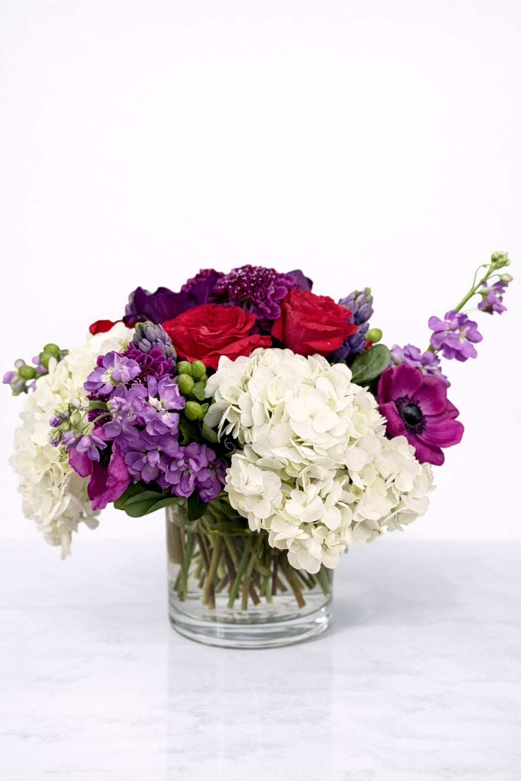 Mixed bouquet of red, white, and purple flowers in a clear glass vase