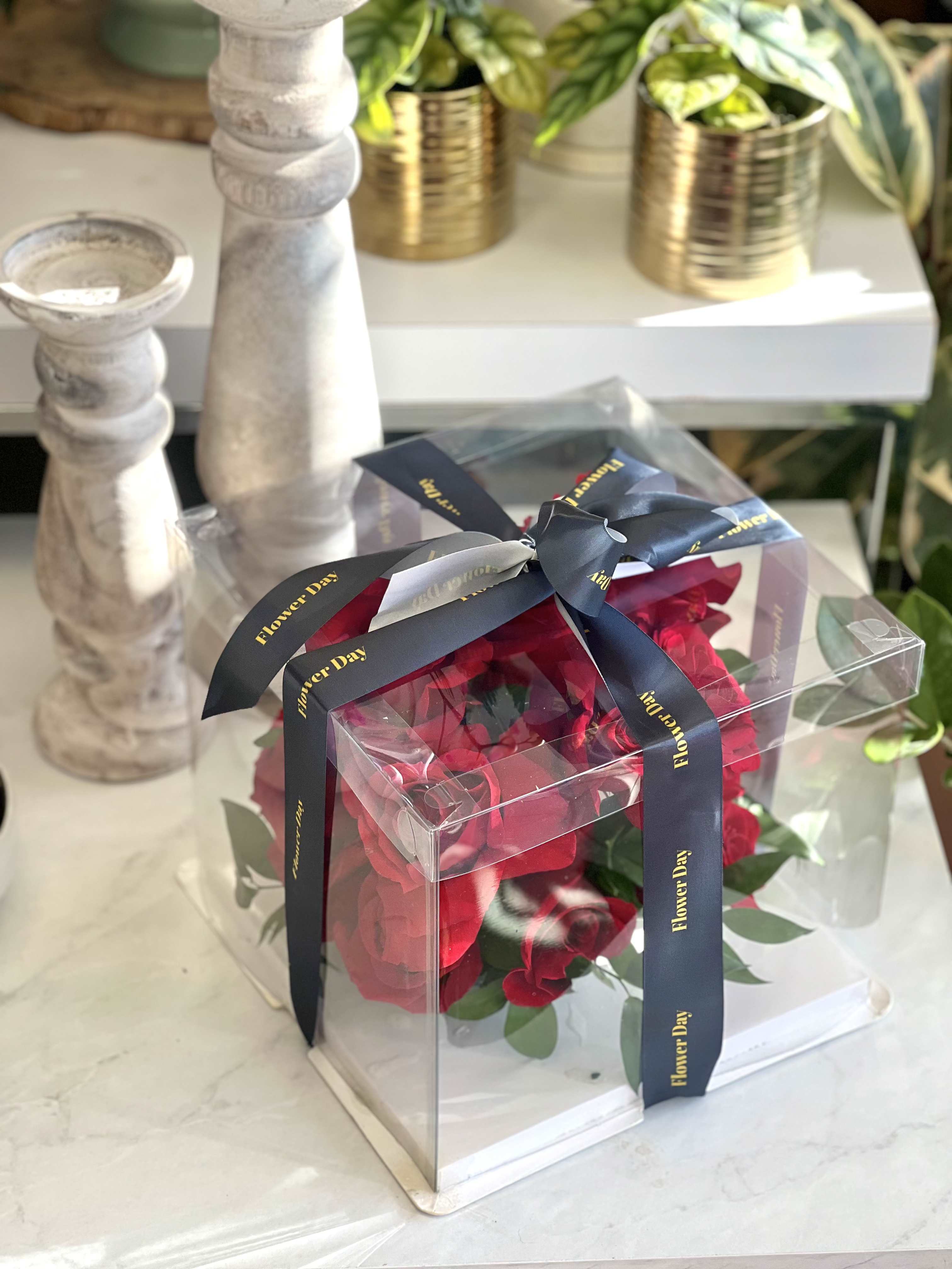 Red roses in a clear gift box tied with a dark ribbon