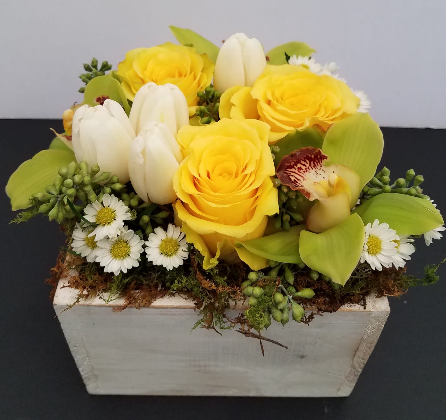 Yellow roses and white tulips in a white rectangular planter
