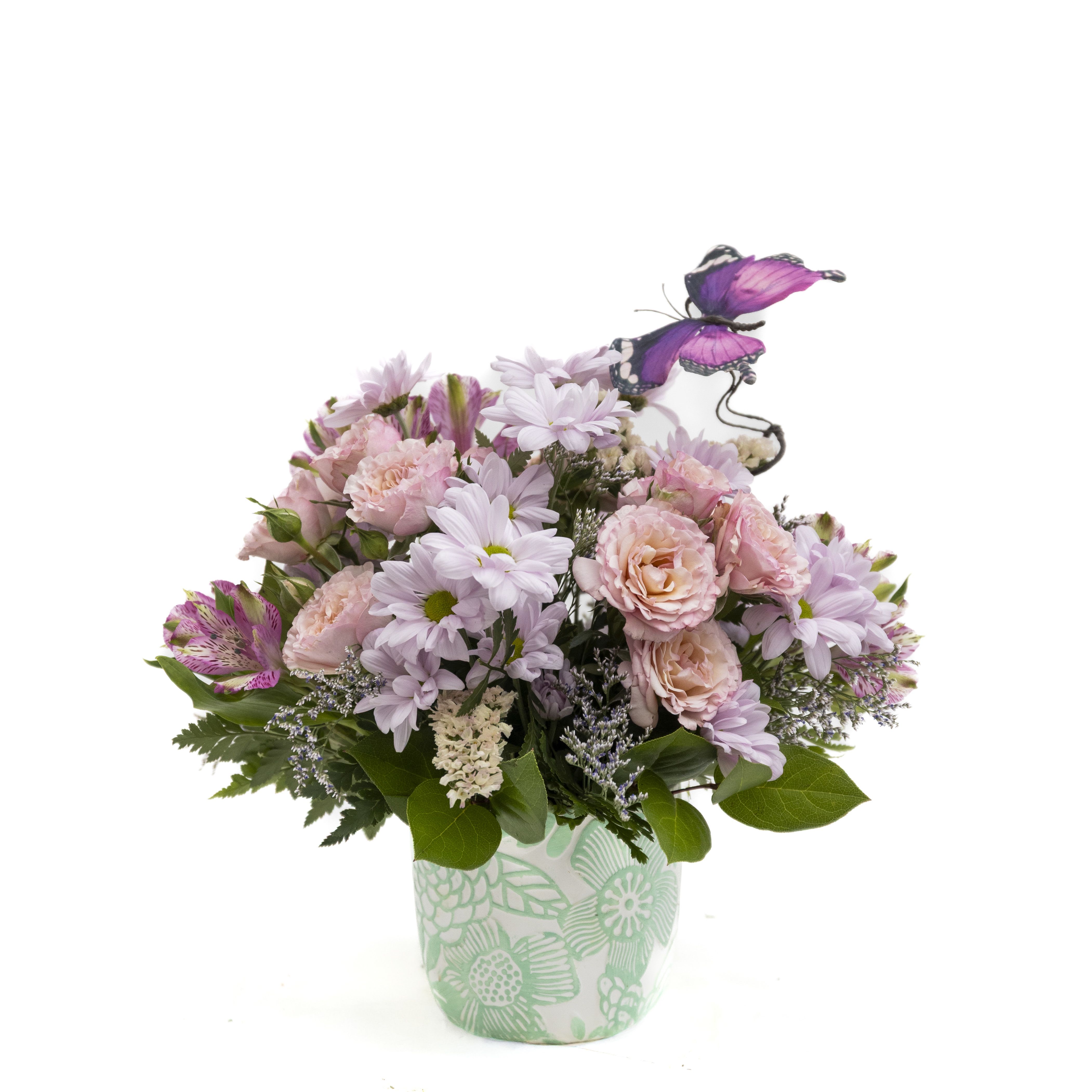 Petal Daydream - Soft, romantic, and full of charm, Petal Daydream is a delicate arrangement that feels like a stroll through a blooming spring garden. Blush pink spray roses and ruffled blooms are paired with gentle lavender daisies and touches of variegated alstroemeria, creating a soothing pastel palette. Lush greenery and airy accents add natural movement, while a graceful butterfly detail brings a whimsical, uplifting touch.  Designed in a mint-patterned container, this arrangement is perfect for celebrating life’s sweet moments—whether it’s a birthday, a thank-you, or simply a gesture to brighten someone’s day. Light, lovely, and full of personality, it’s a gift that feels both thoughtful and enchanting.