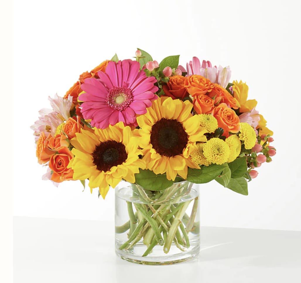 Bright mixed bouquet with sunflowers, gerbera daisies, and orange roses in a glass vase