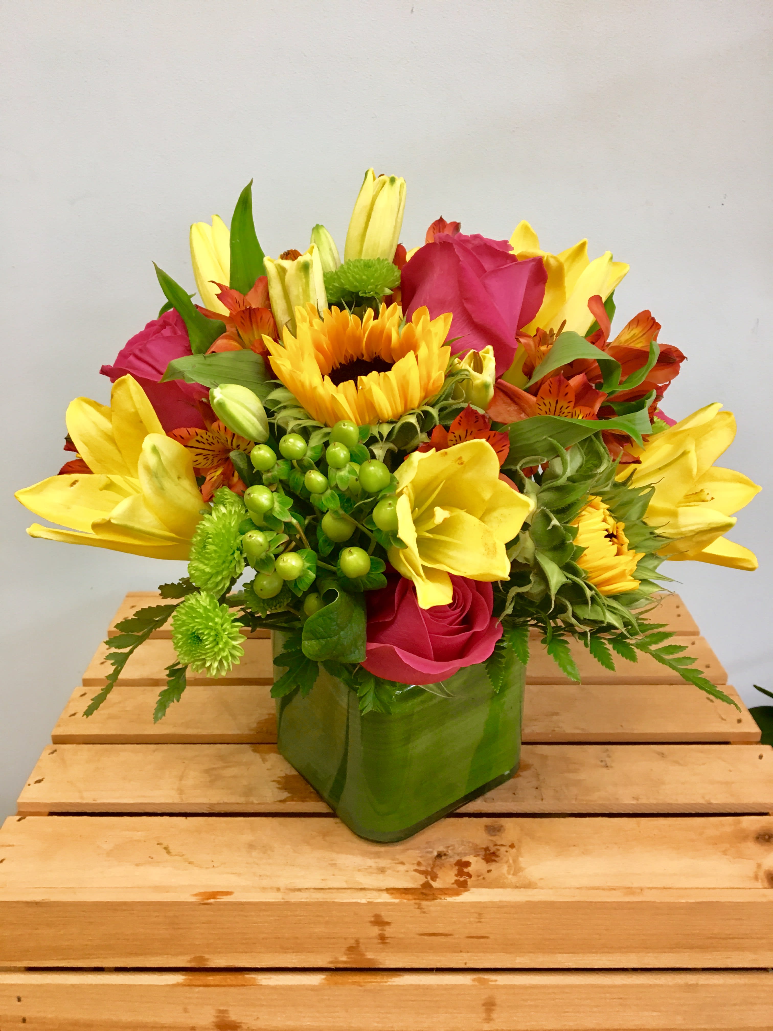 Bright mixed bouquet with sunflowers, yellow lilies, and pink roses in a green vase