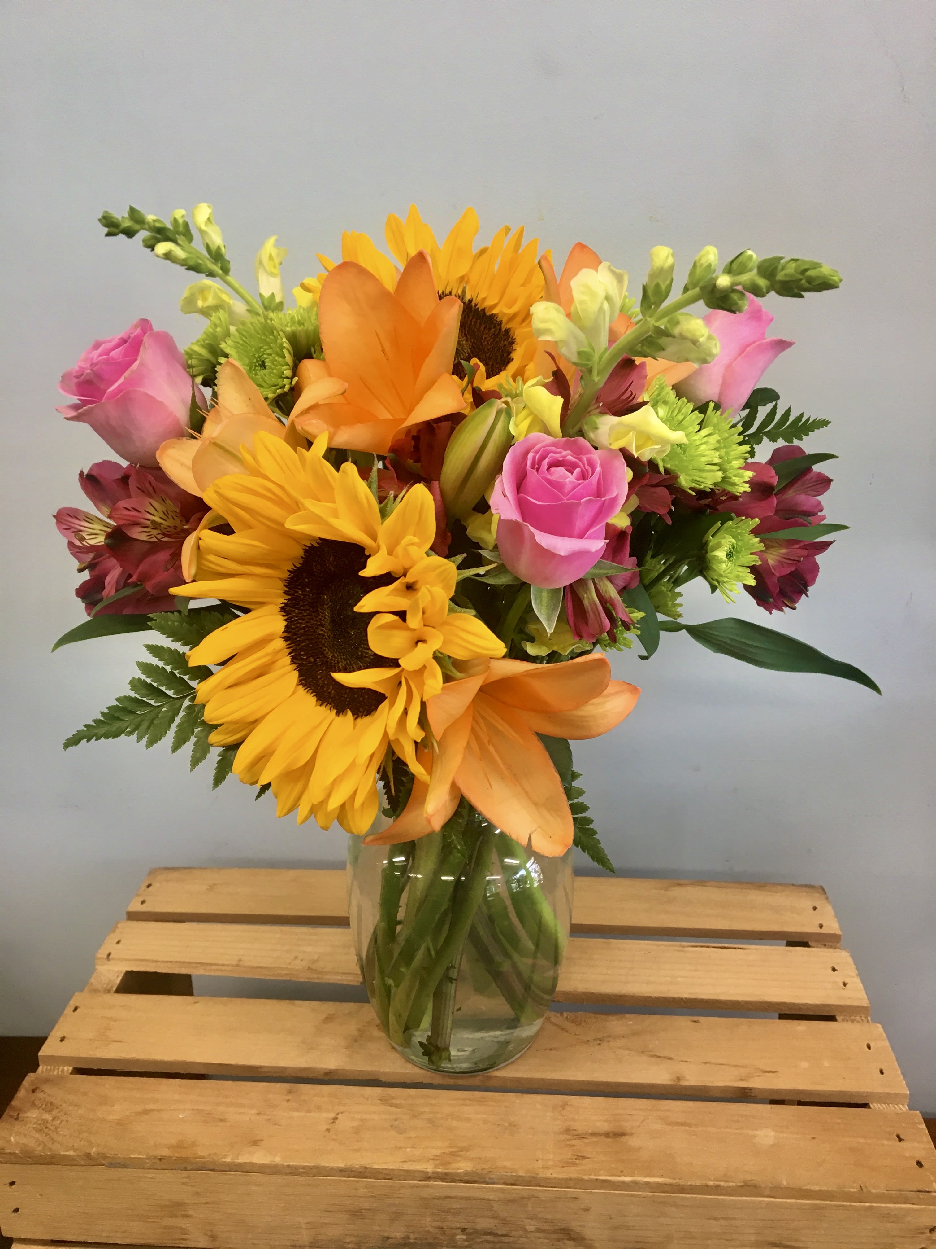 Mixed bouquet of sunflowers, pink roses, and orange lilies in a glass vase