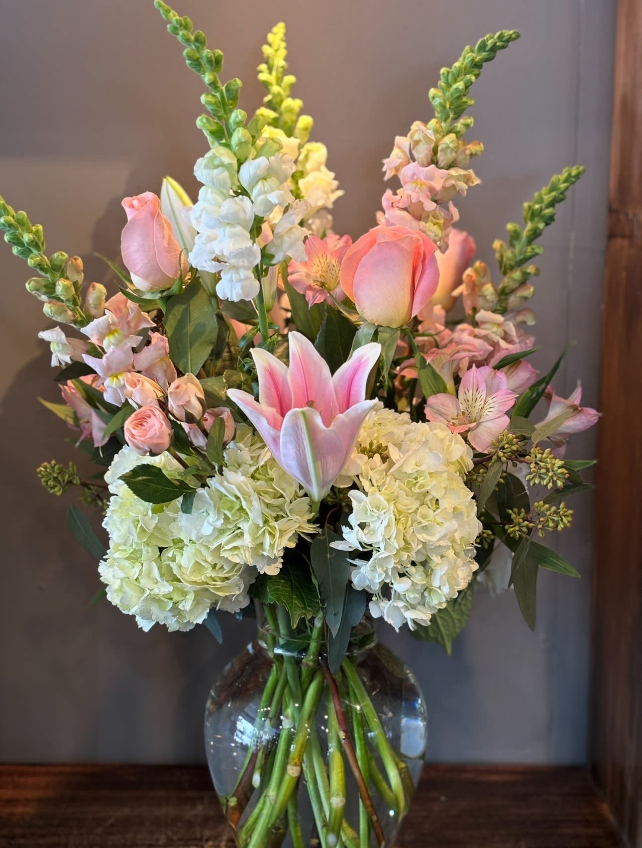 Tall arrangement of pink lilies and roses with white hydrangeas in a clear glass vase