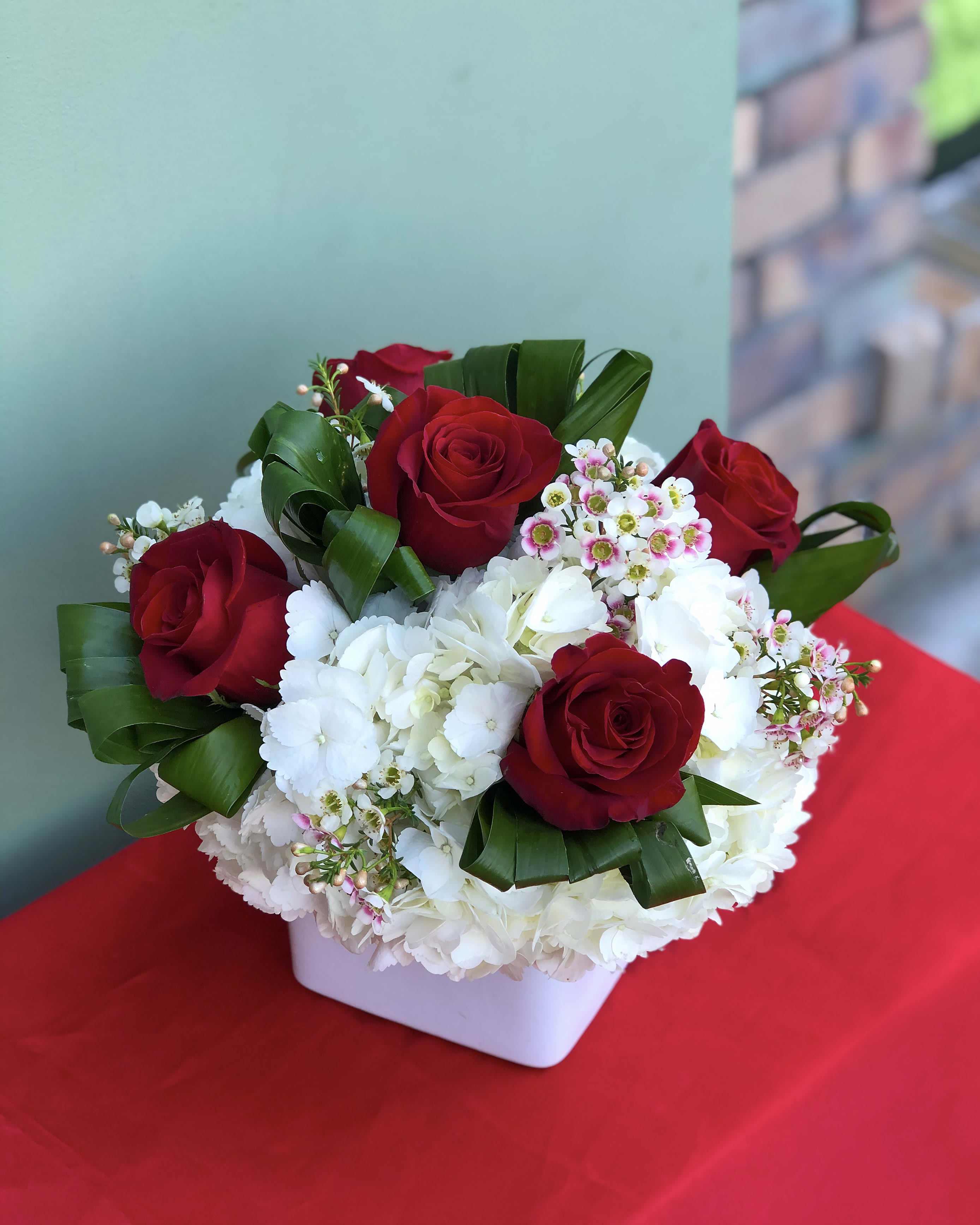 Red roses and white hydrangeas in a white square vase
