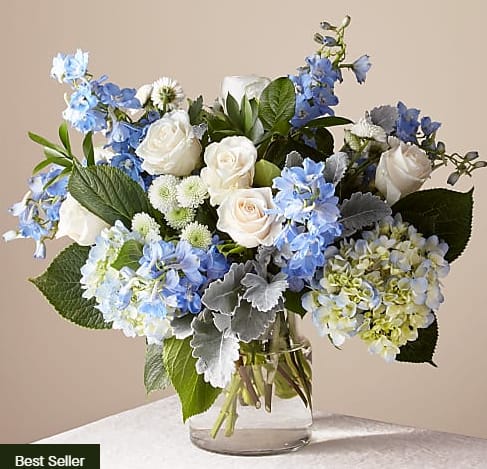 Arrangement of white roses, blue hydrangeas and blue delphinium in a clear glass vase