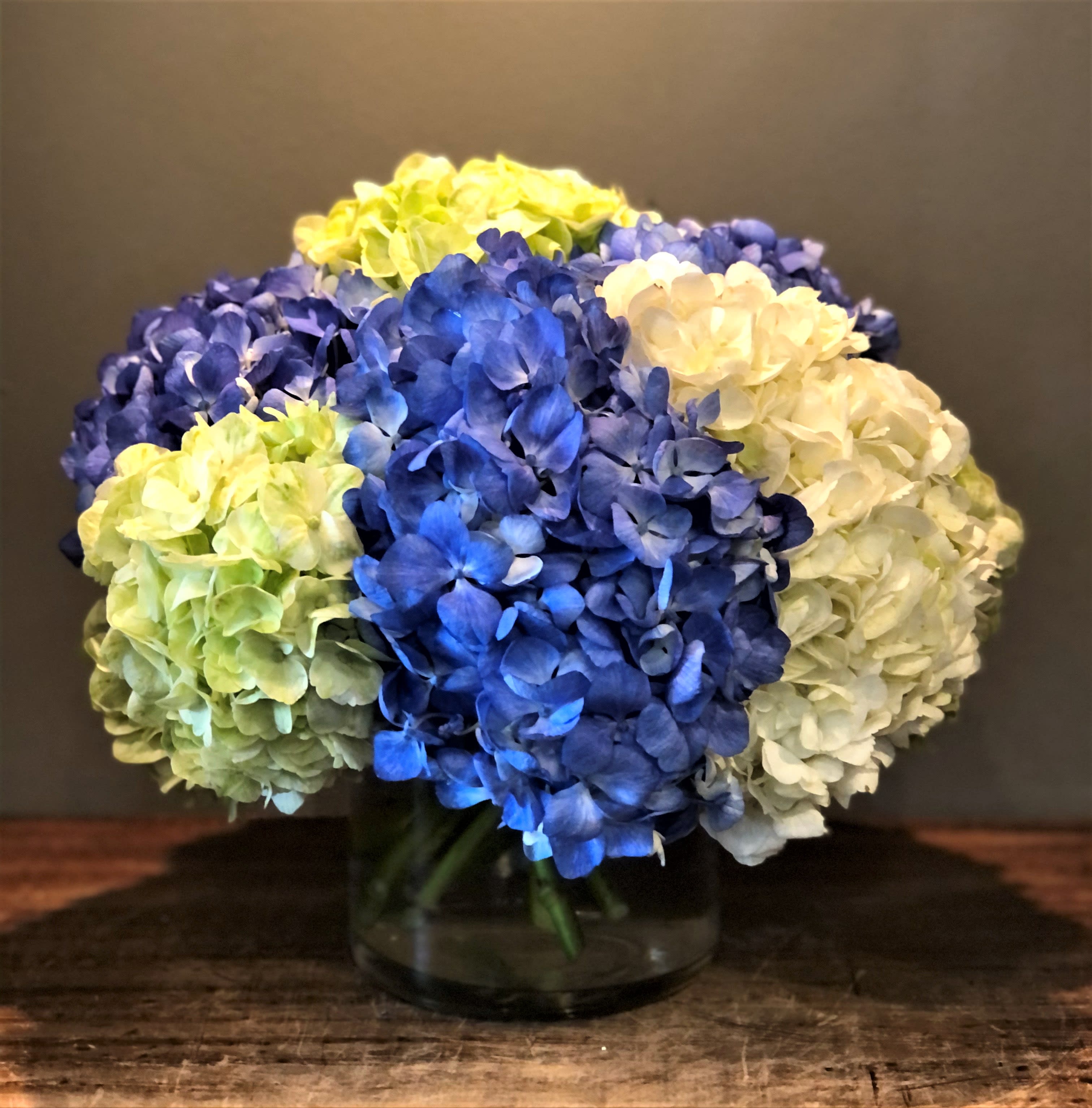 Blue, white, and green hydrangeas in a glass vase