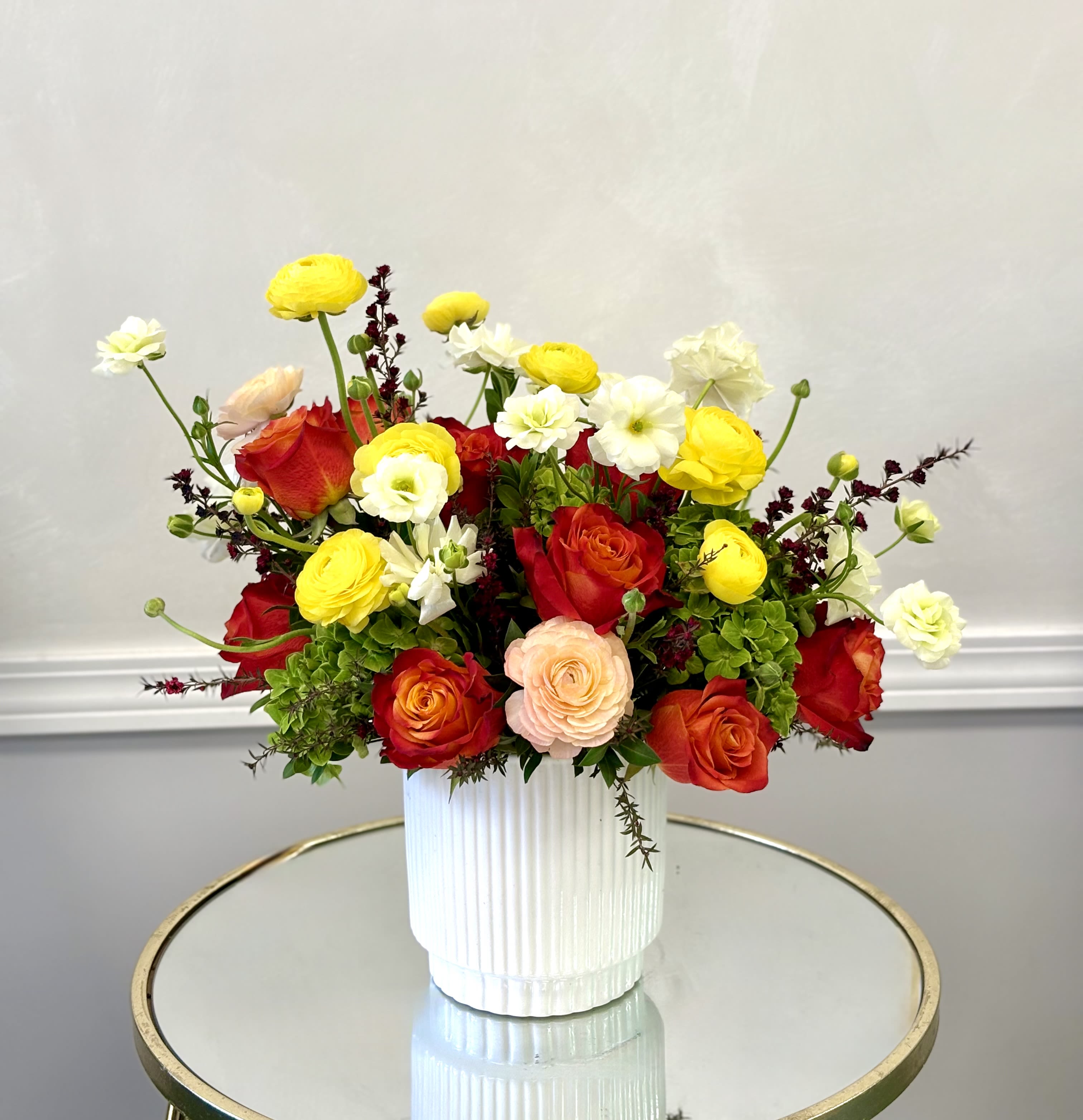 Warm Garden Symphony By VLM Flowers - Layers of red, coral, and golden blooms come together in a rich, textured arrangement that feels both elegant and full of life.