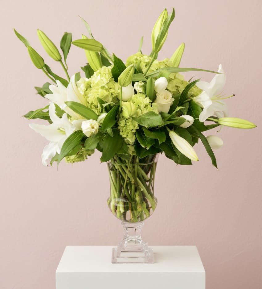 White lilies and green hydrangeas arranged in a clear pedestal vase