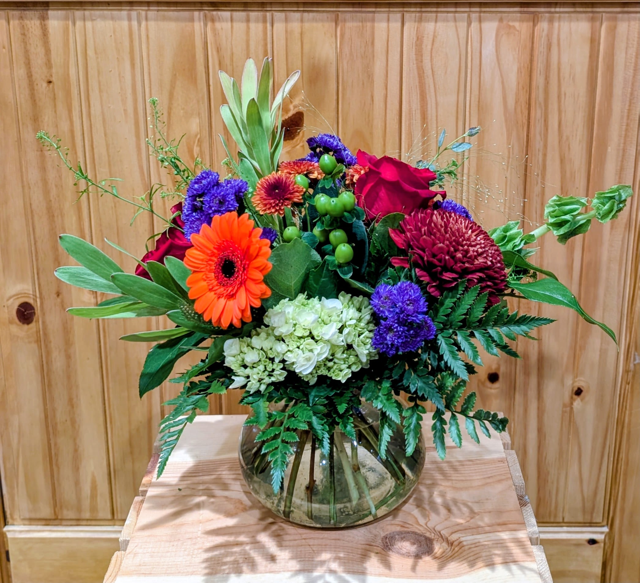 Colorful Dream - GLASS VASE INCLUDES ORANGE GERBER DAISY, MUM, HYDRANGEA, RED ROSES, HYPERICUM, BELLS OF IRELAND, WAX FLOWERS AND GARDEN OF GREENS.