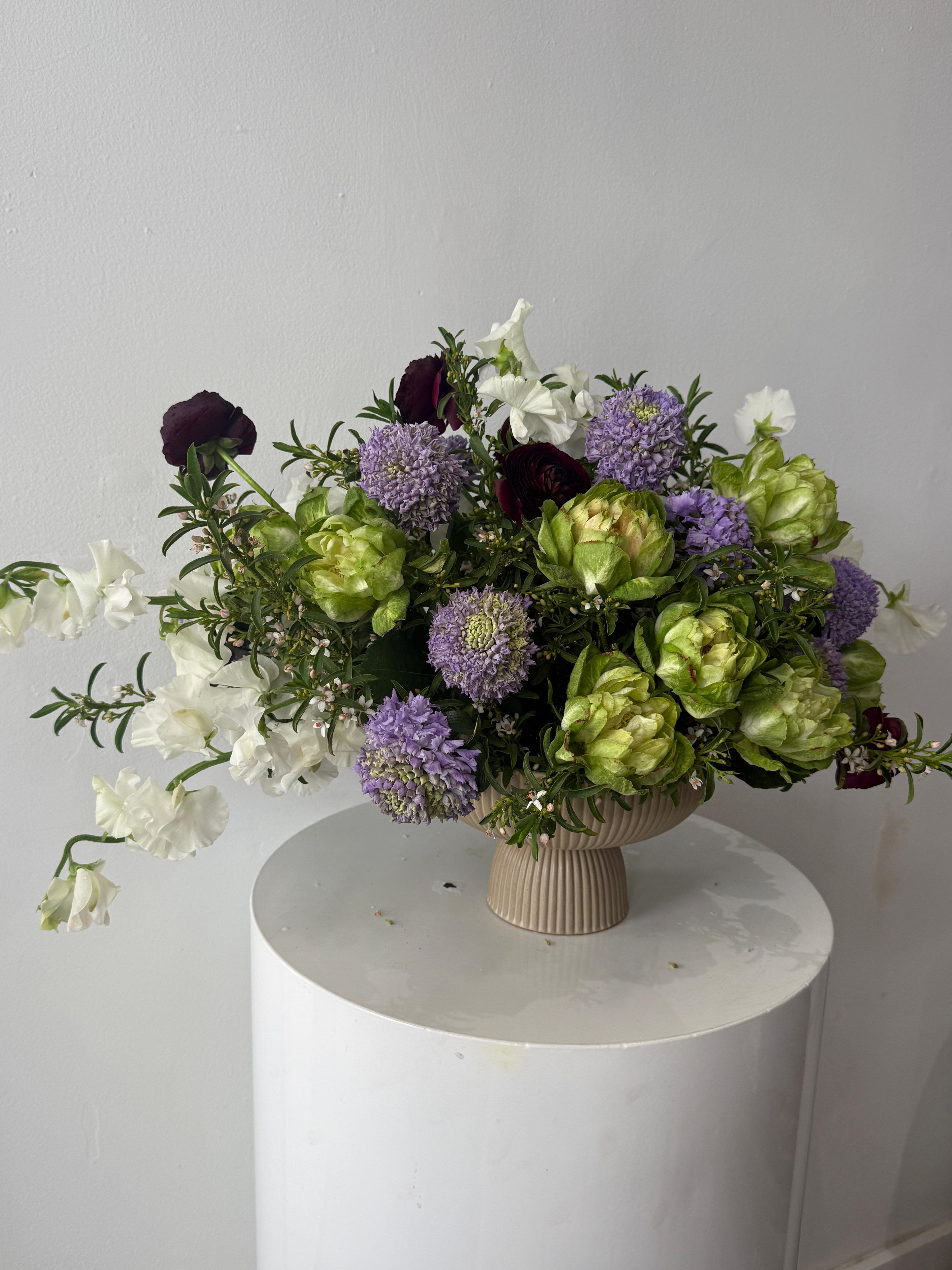 Lavender Lemonade - This arrangement feels like a playful little party in bloom—soft lavender scoops mingle with creamy white sweet pea, while pops of deep burgundy peek through like a wink. Fresh chartreuse veggie give it a zesty, almost fizzy energy.